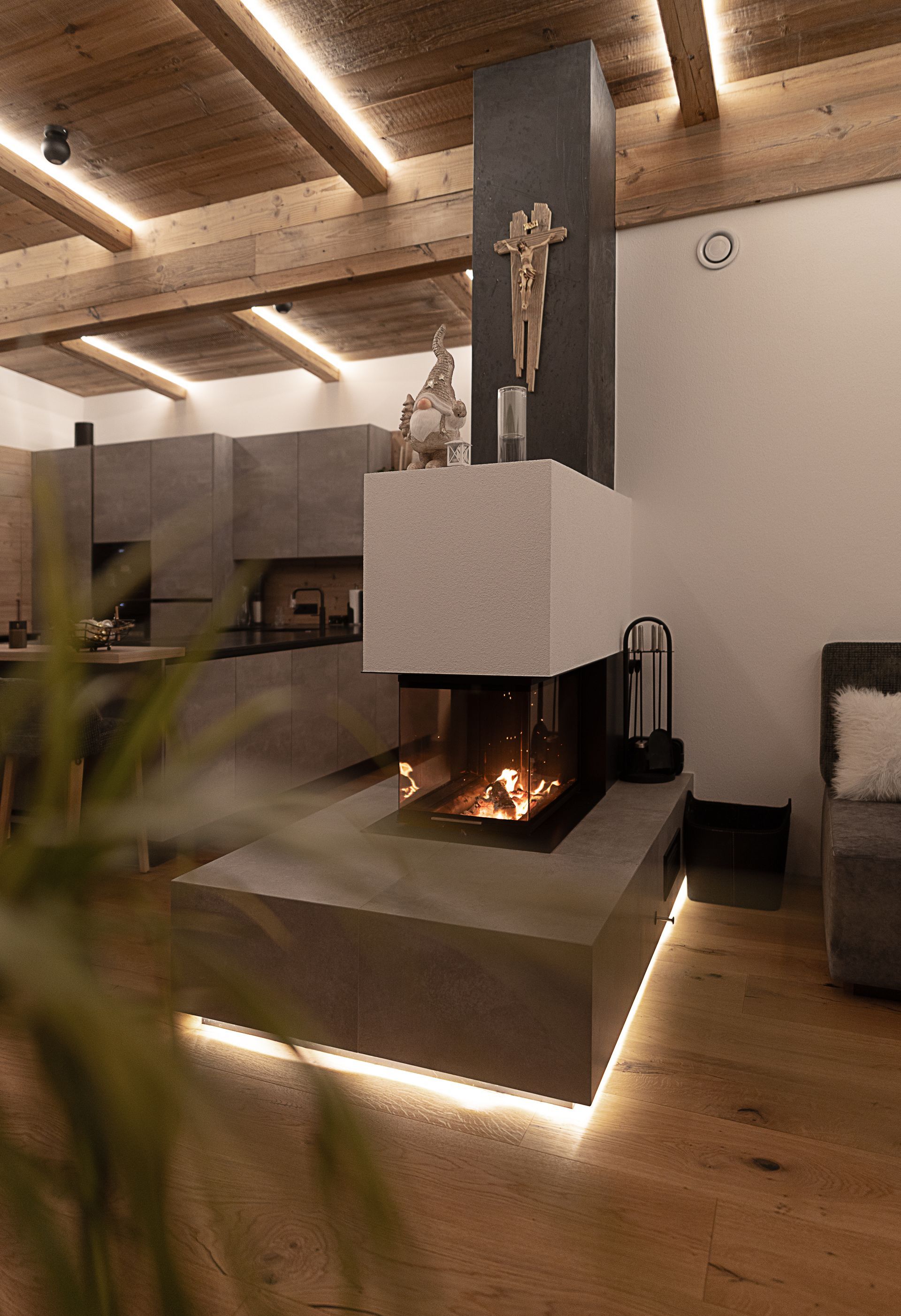 Modernes Wohnzimmer mit freihängendem Kamin, warmen Holzbalken und sanfter Akzentbeleuchtung