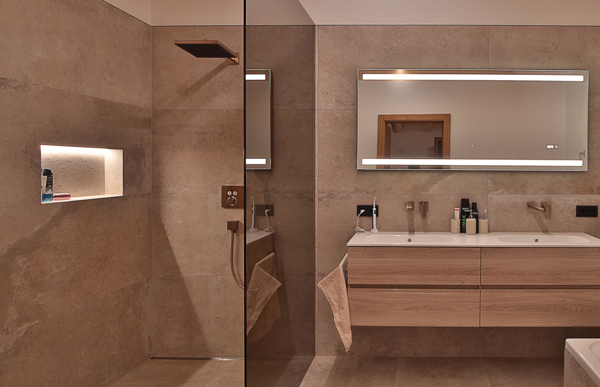 Modernes beigefarbenes Badezimmer mit Glasdusche, Doppelwaschtisch und beleuchtetem Spiegel