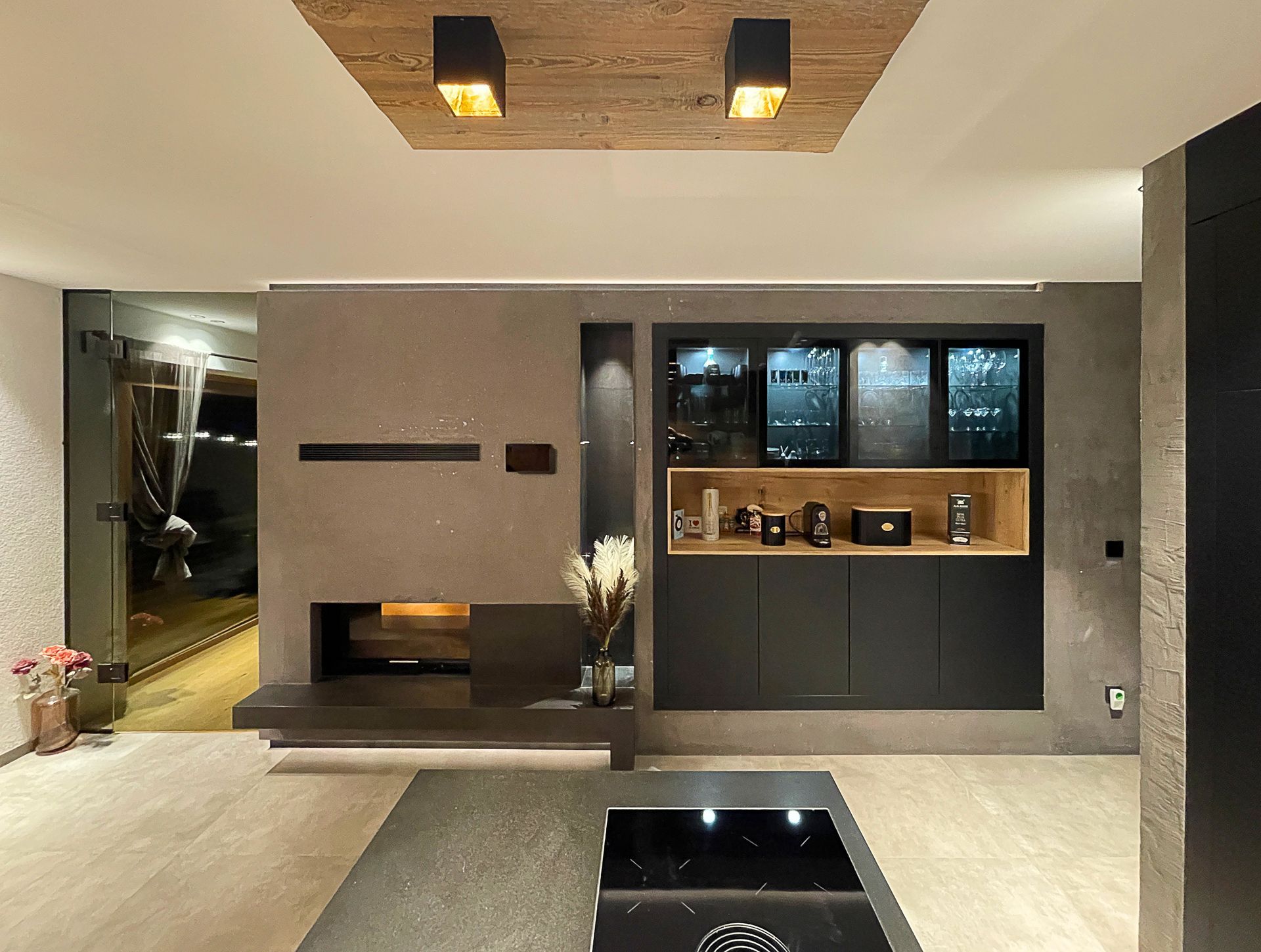 Modernes Wohnzimmer mit grauer Kaminwand, schwarzen Schränken, warmen Holzregalen und Einbauleuchten