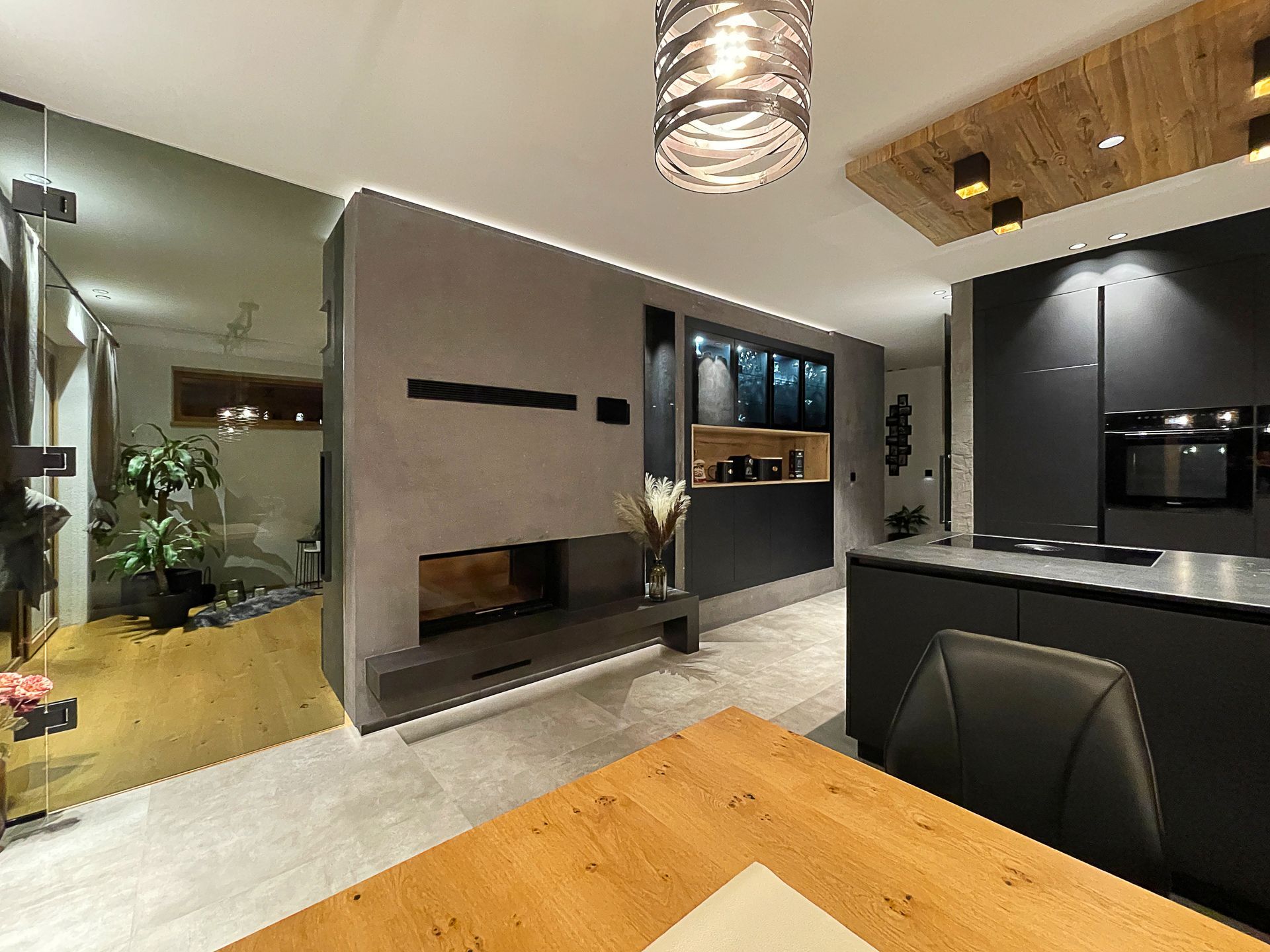 Modernes Wohnzimmer mit eingebautem Kamin, Wandfernseher, schwarzen Schränken und einem Esstisch aus Holz.