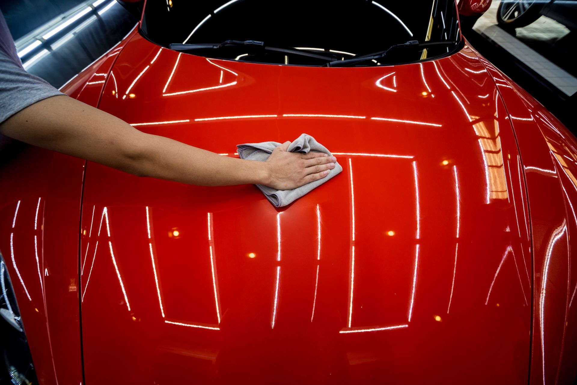 A person is cleaning the hood of a red car with a cloth.