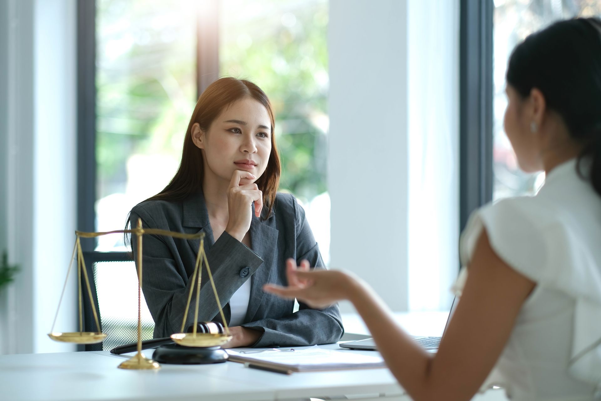 Lawyer speaking with a client across a desk in a bright office, with scales of justice nearby