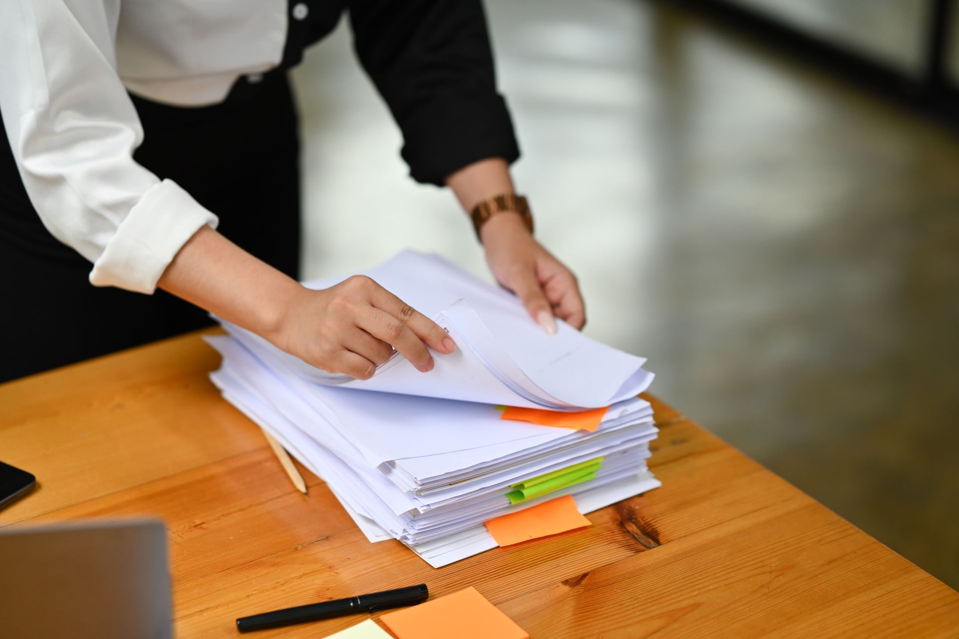 Hands sorting a stack of papers on a wooden desk
