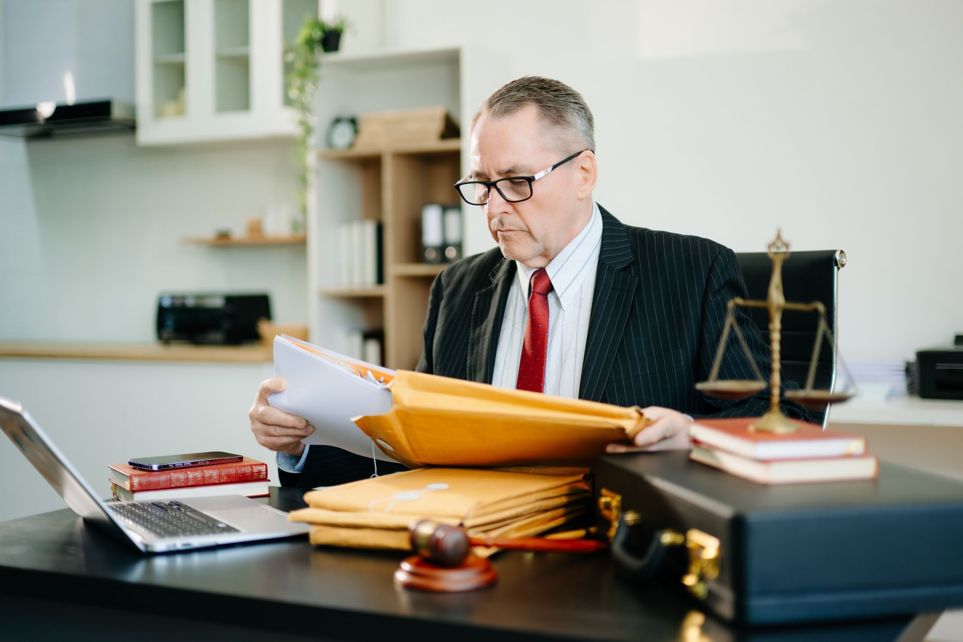Lawyer reviewing documents at a desk with files, scales, and a gavel in an office