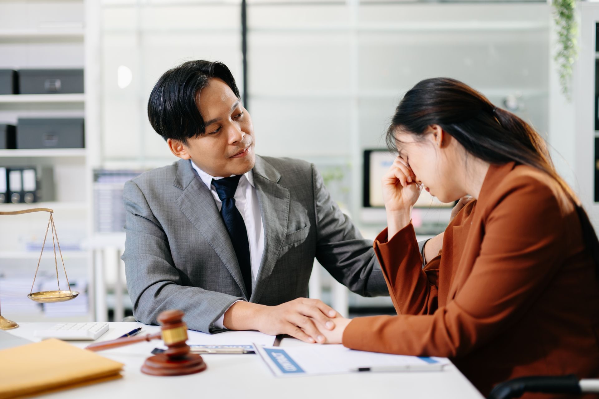 Attorney consulting with a distressed client at a desk in an office, with a gavel visible nearby.
