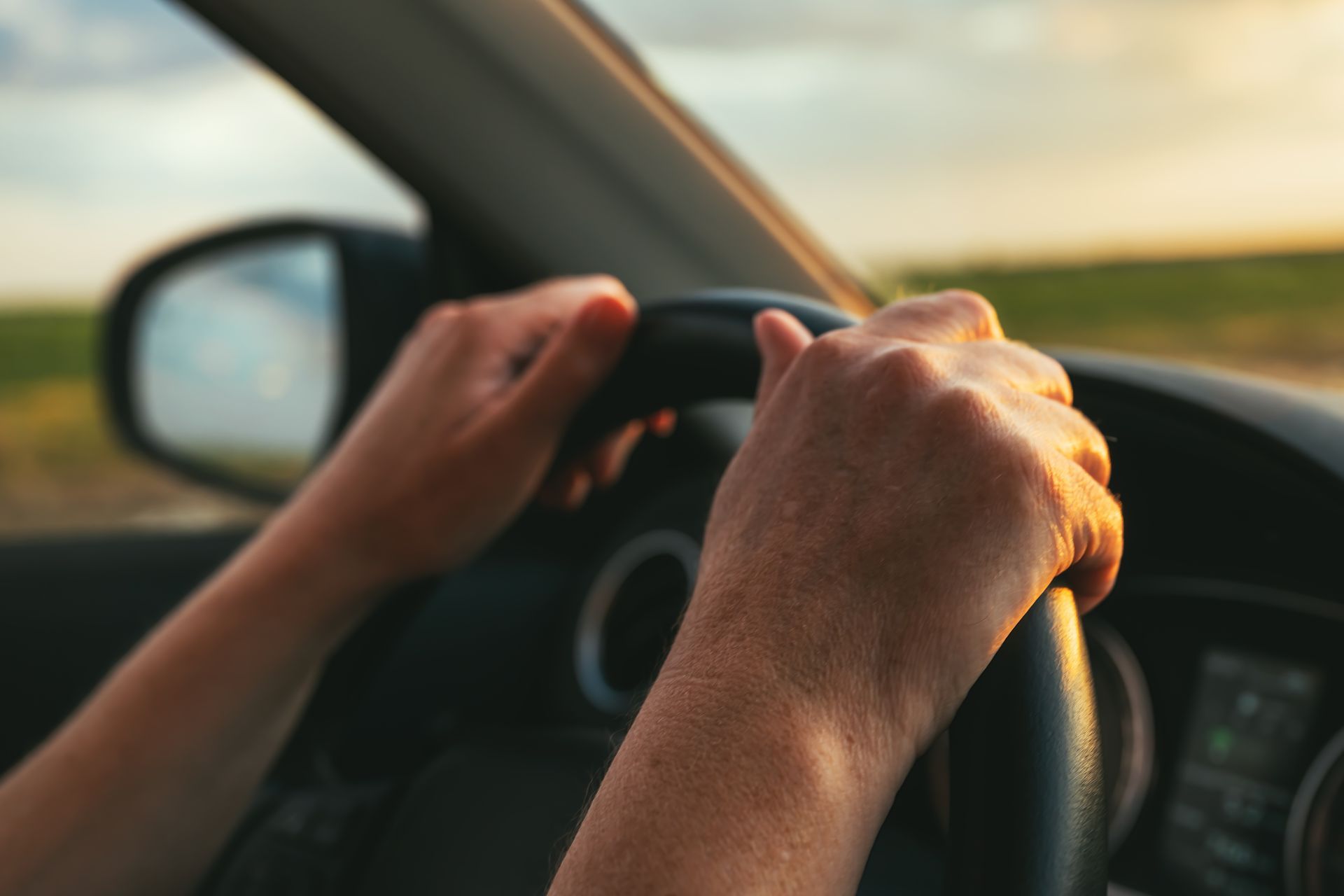 Close-up view from behind the steering wheel as a person drives along a road at sunset.