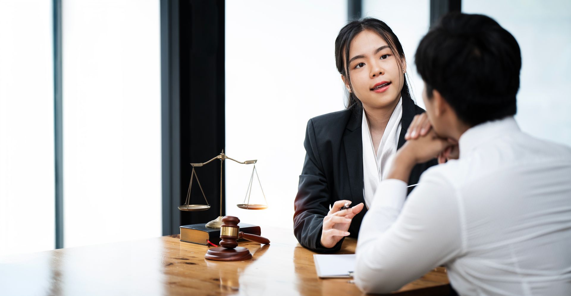 Two people in a meeting at a desk, with a small scale and gavel in a bright office.