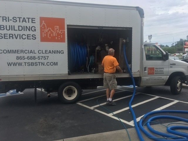 Man in orange shirt with hose at Tri-State Building Services truck in a parking lot.