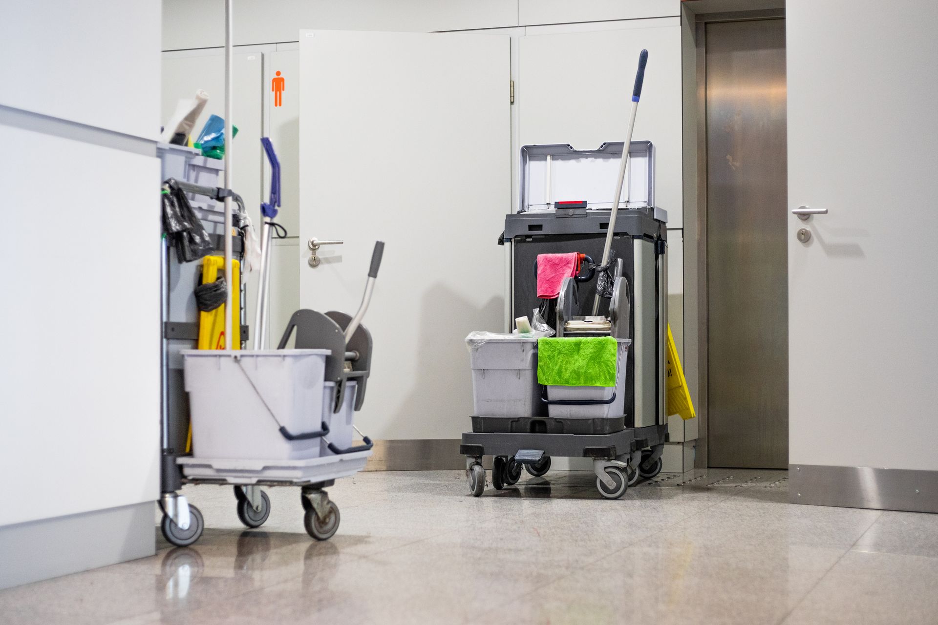 Two cleaning carts in a hallway, one with a bucket, the other with supplies and mop.