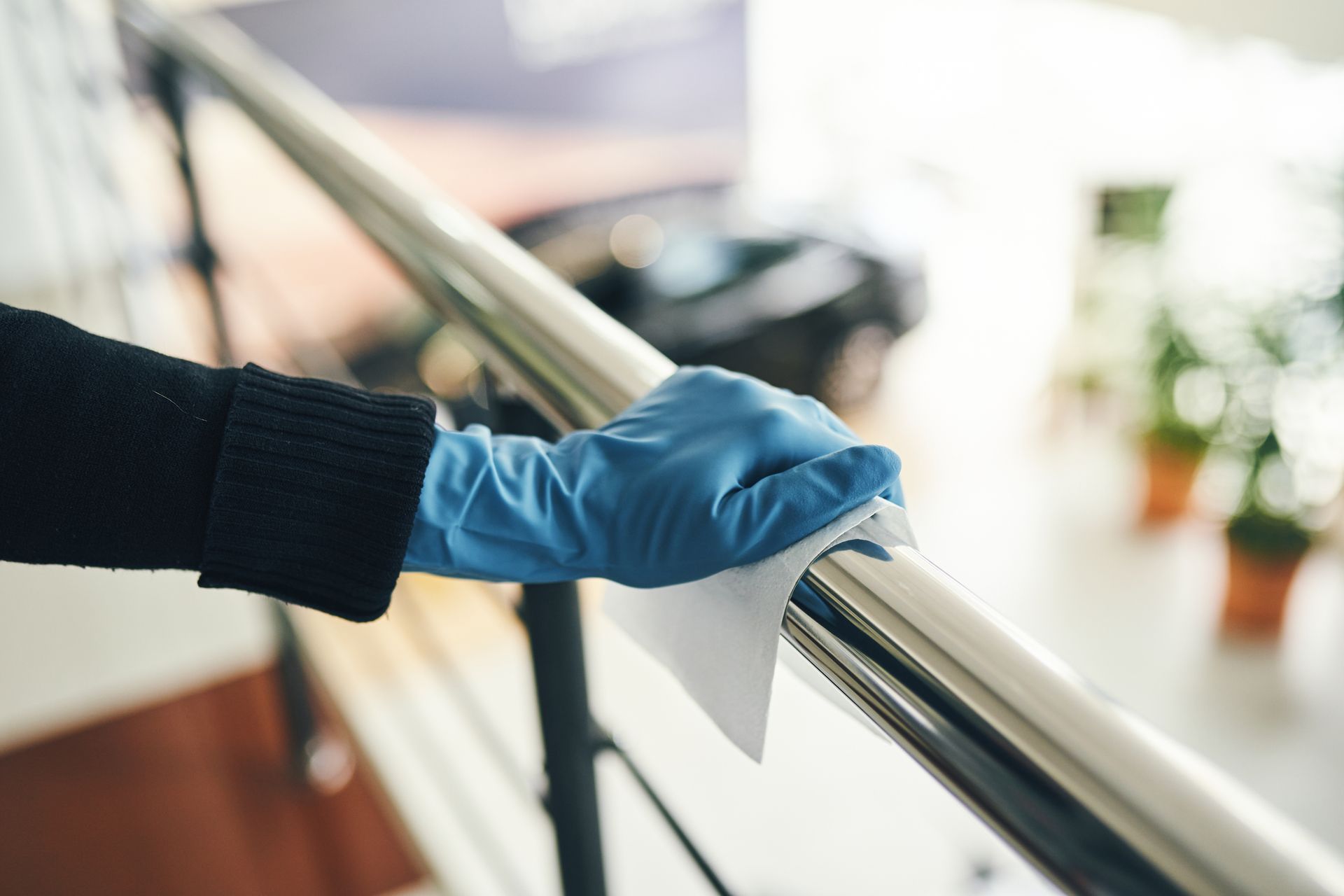 A person wearing gloves wipes a metallic railing with a cloth in a modern commercial space.