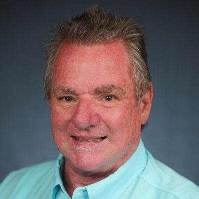 Headshot of a smiling man in a light blue shirt against a gray background