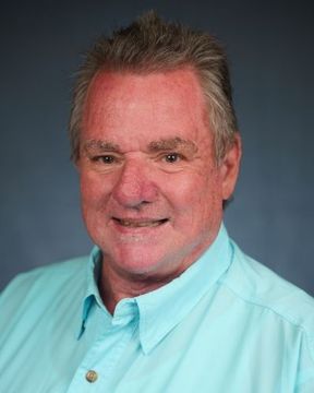 Smiling man in a light blue shirt against a dark blue background.