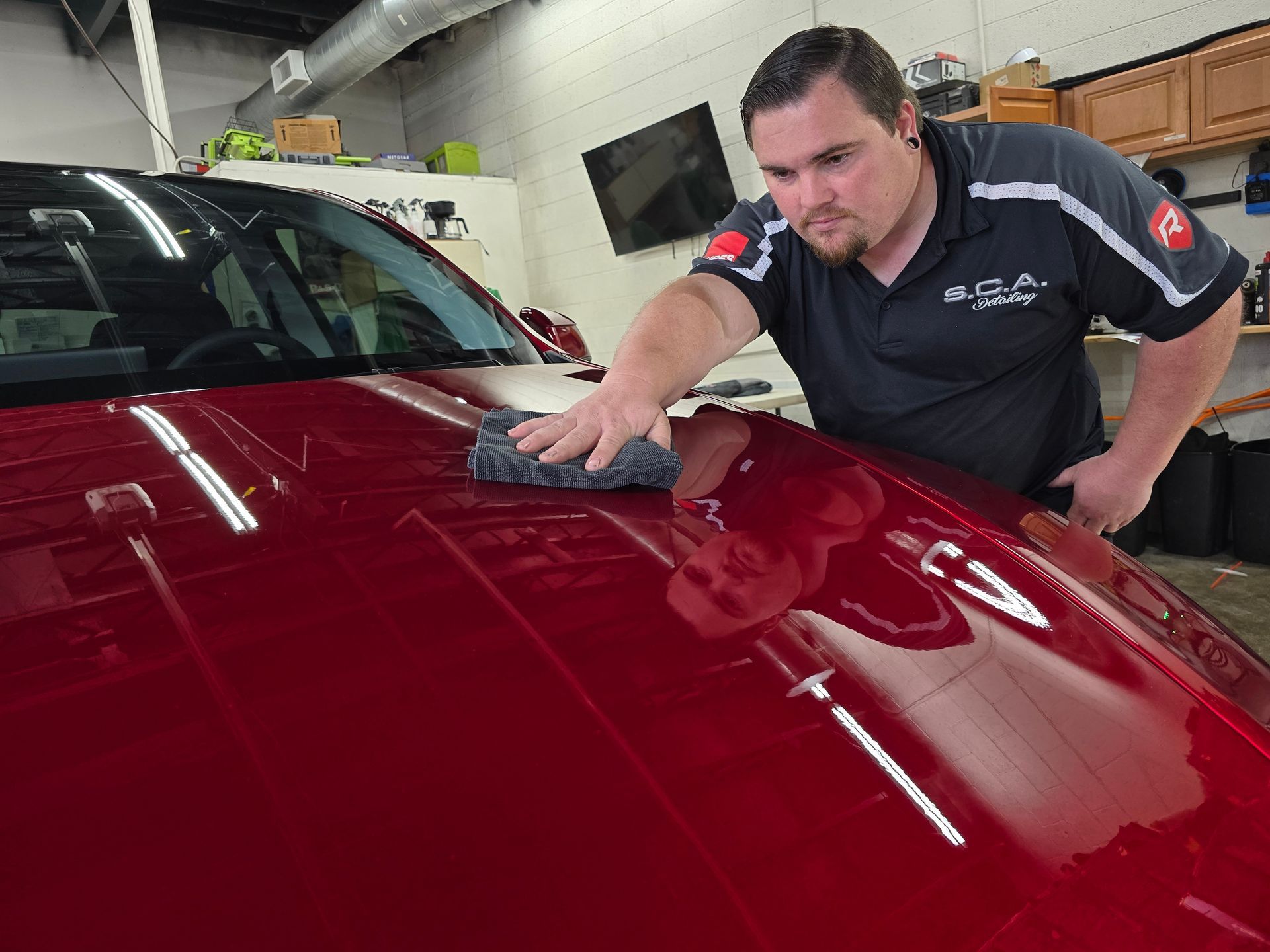 Man polishing a red car hood in an auto shop with a microfiber cloth