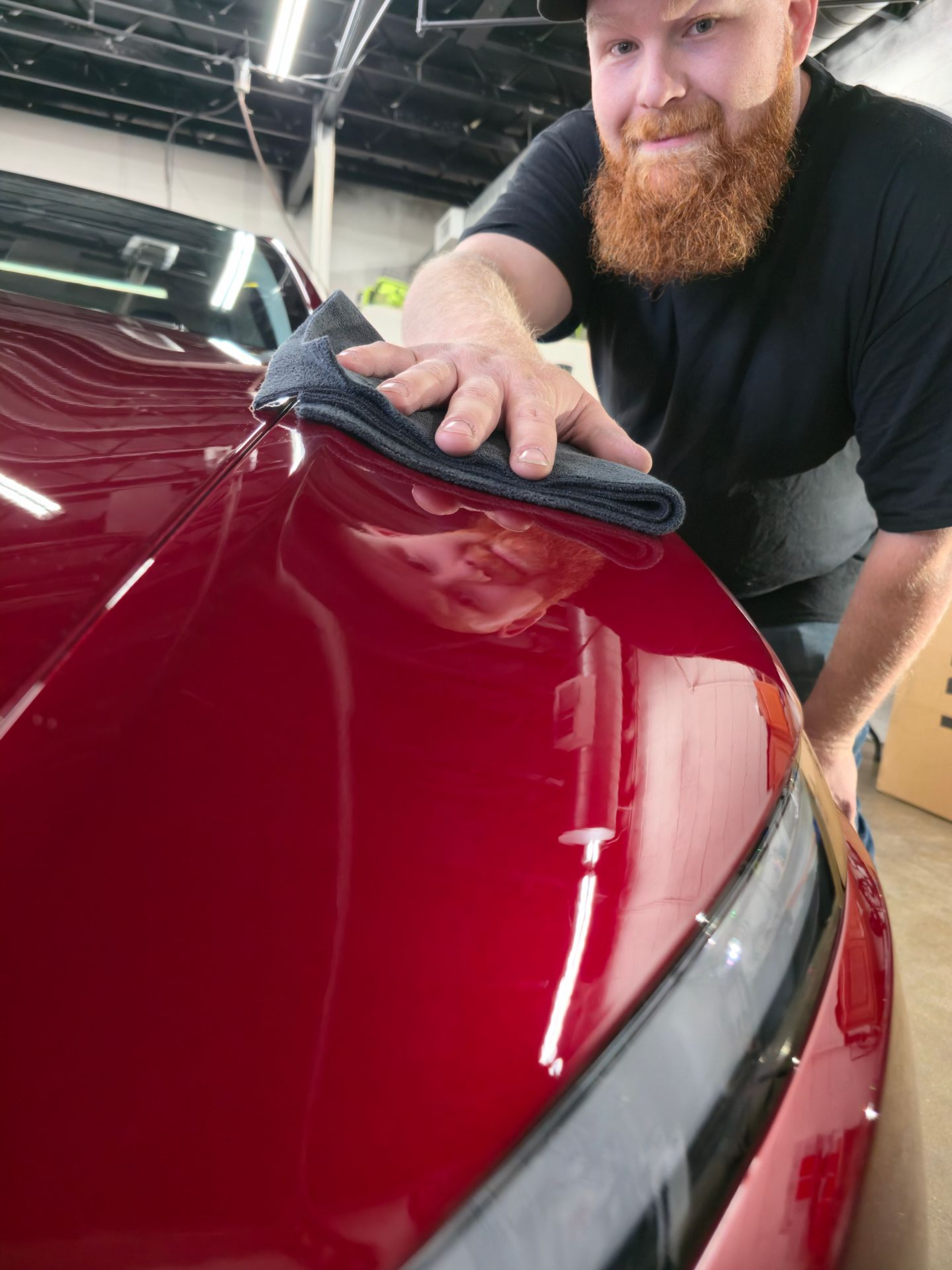 Person wiping a glossy red car hood with a cloth in a workshop