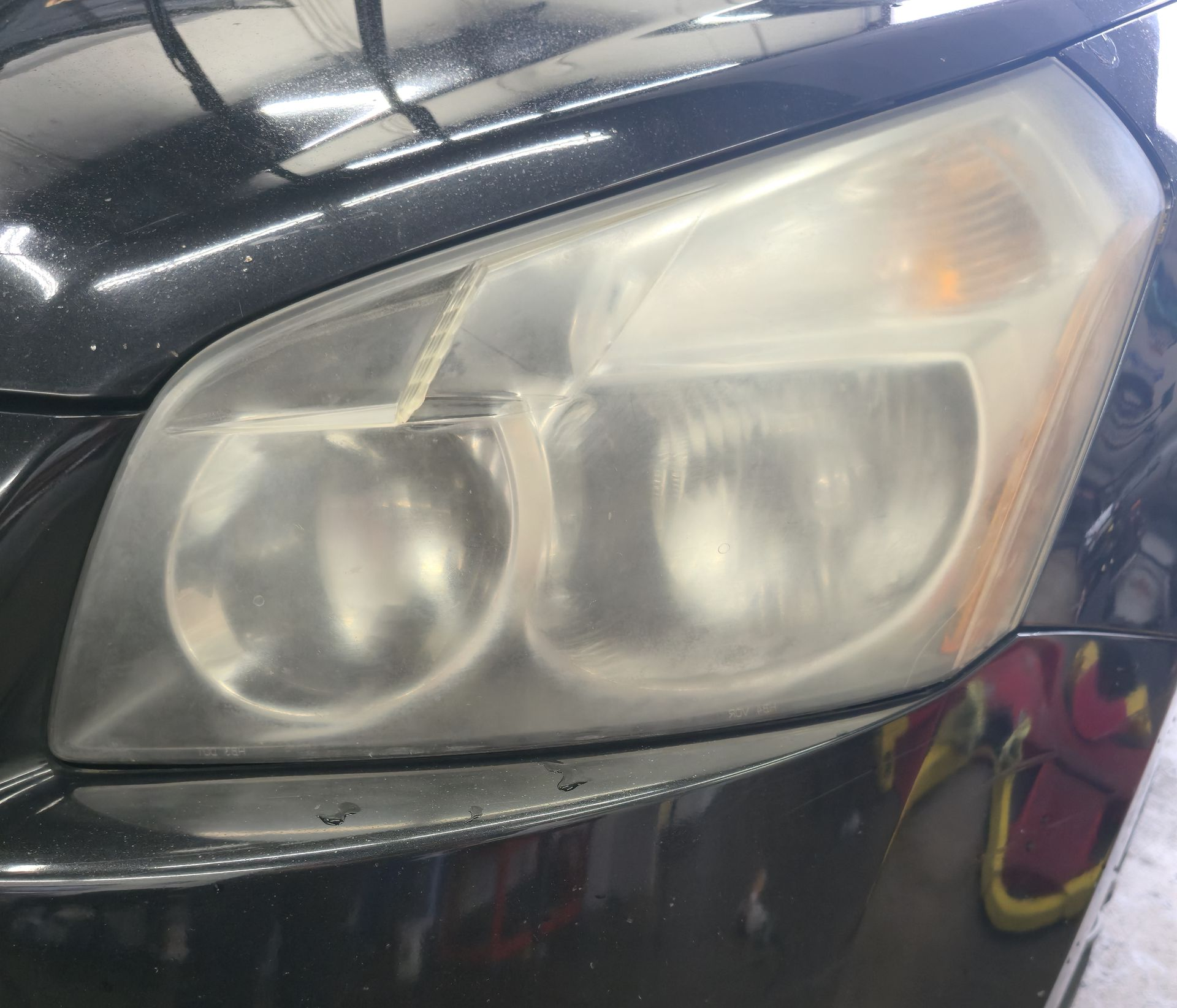 Close-up of a car headlight with cloudy, yellowed lenses on a dark vehicle body