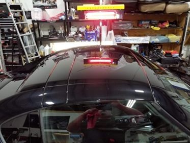Black car roof with red heat lamp, detailing or repair. Workshop setting.