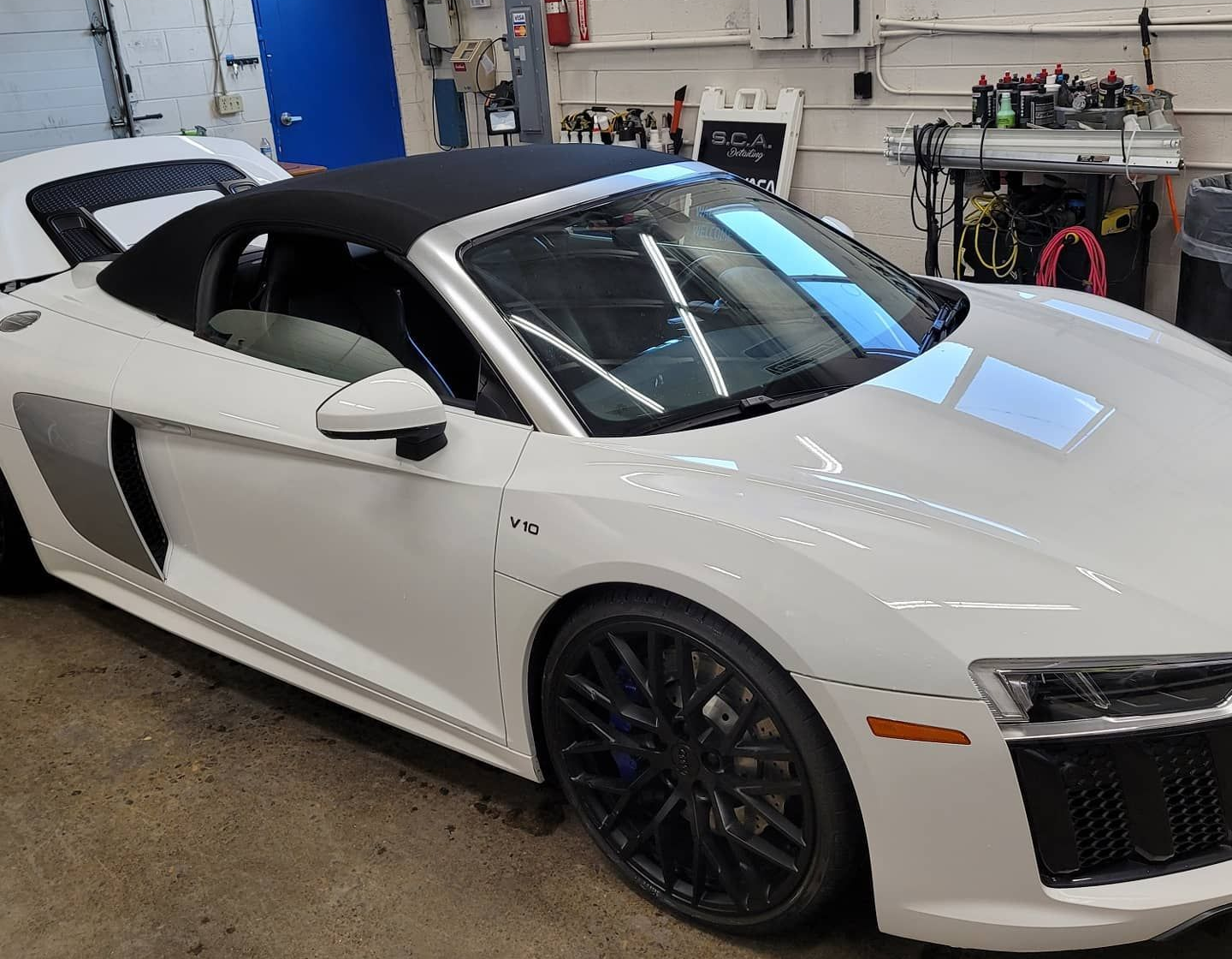 White convertible sports car in a garage, side view with black roof and black rims.