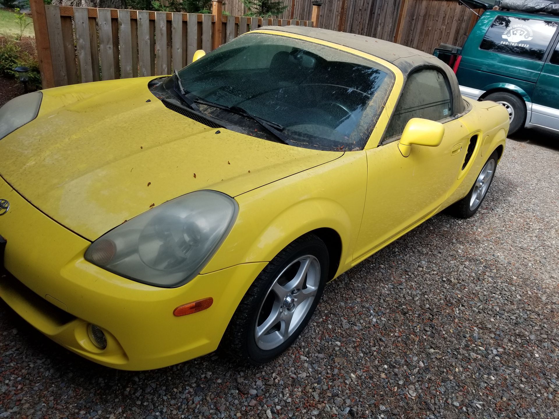 Close-up of a gray sports car with bronze wheels parked outside a garage.