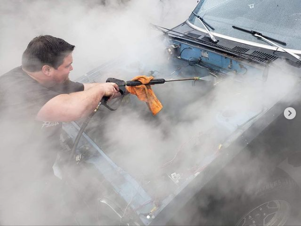 Person washing a car window with a soapy mitt, visible arm tattoo.