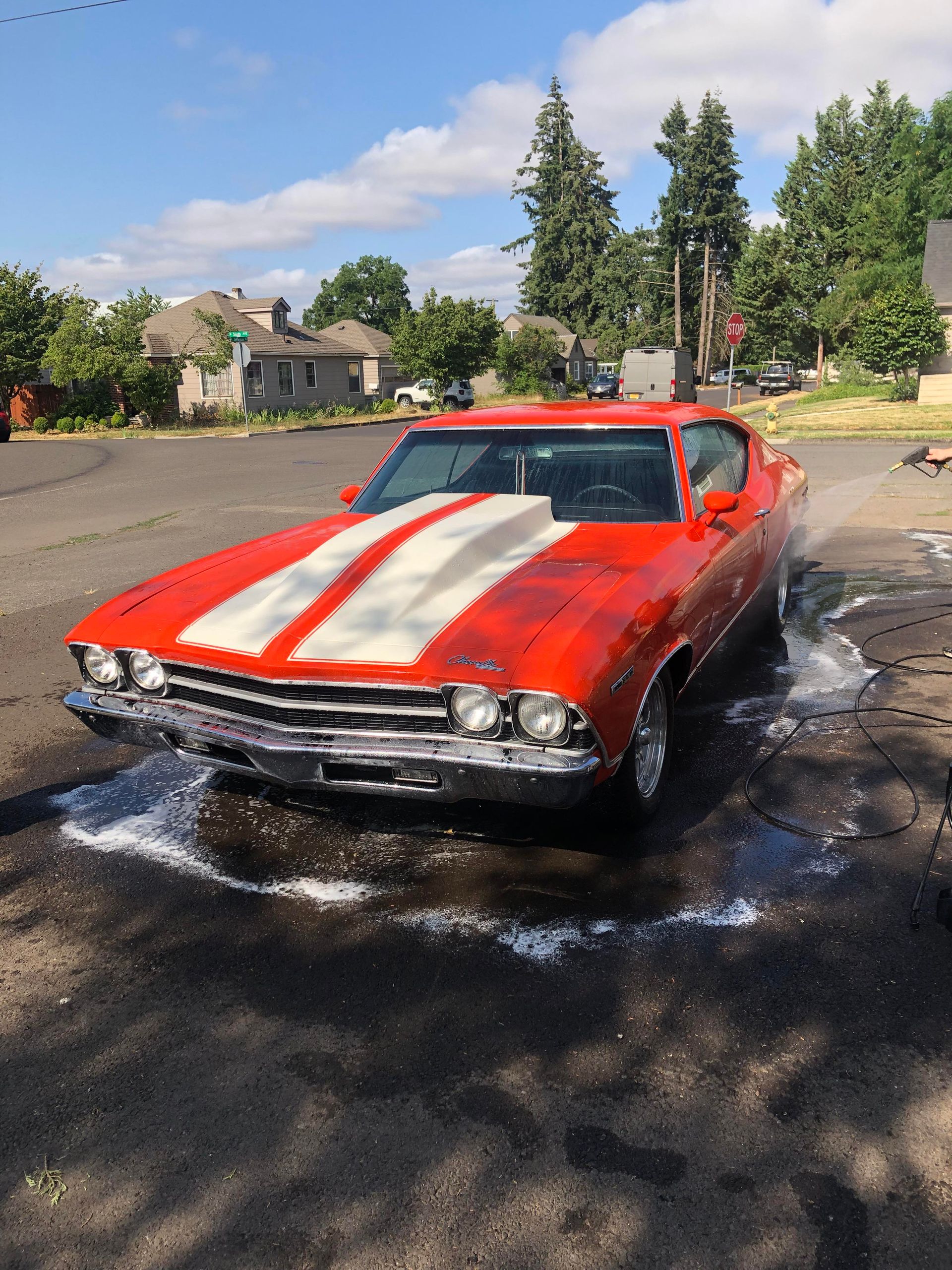 Person washing a car's tire with a soapy sponge on a green grassy lawn.