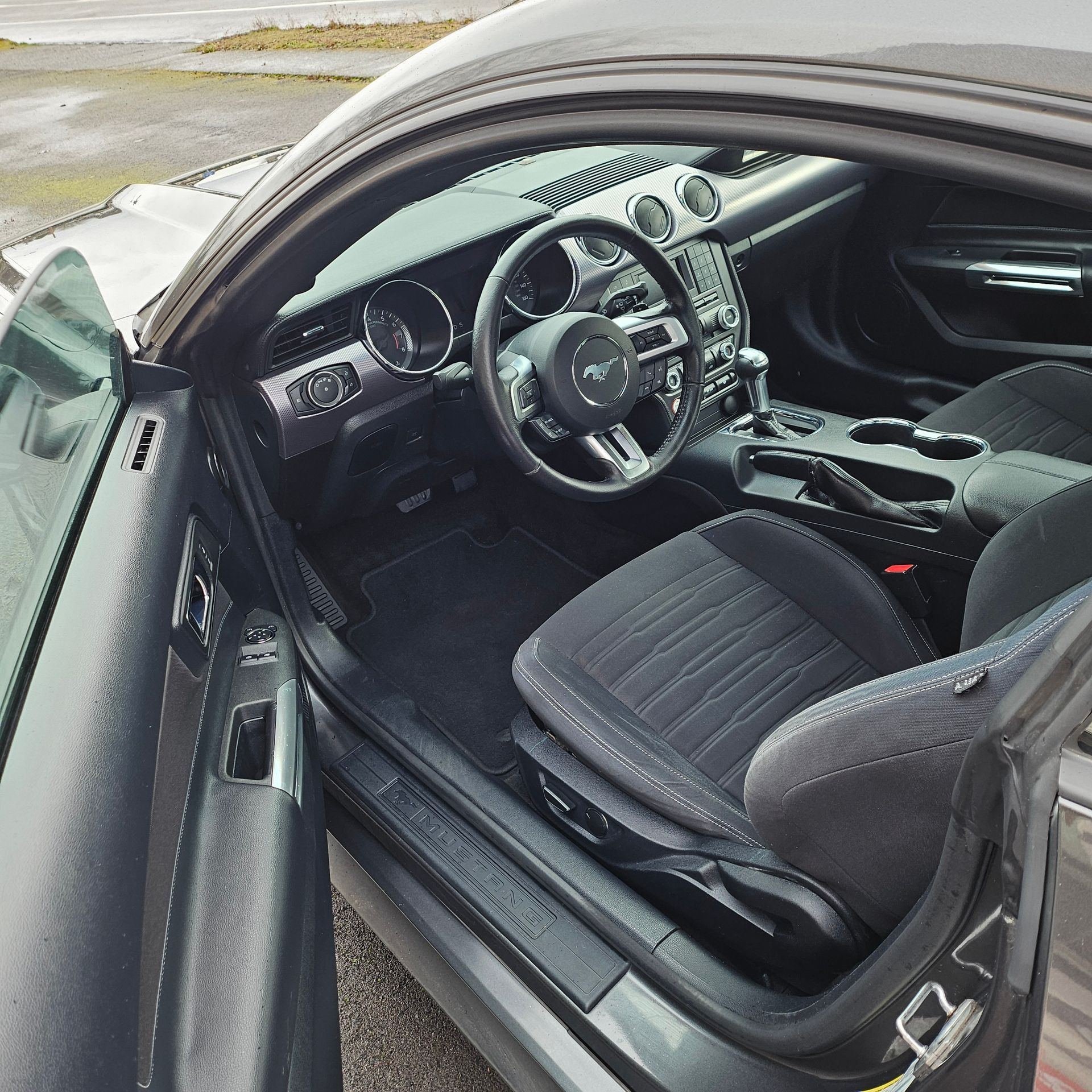 Open driver's door showing a black car interior with steering wheel and front seat.