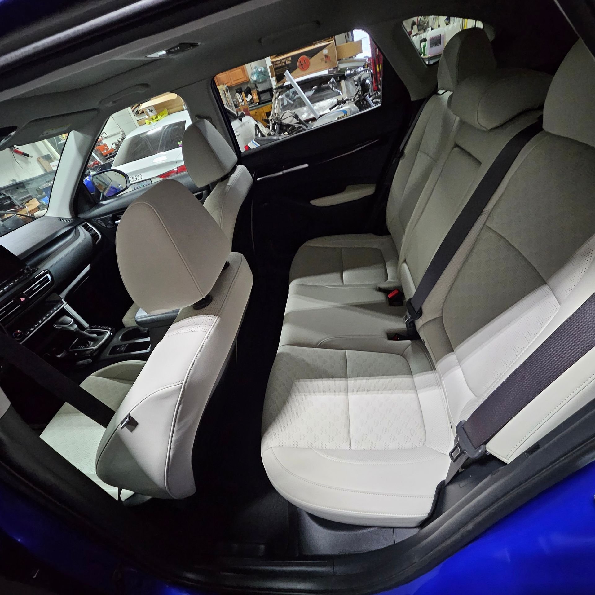 Car interior with beige rear seats and door open, showing the back seat from the side.