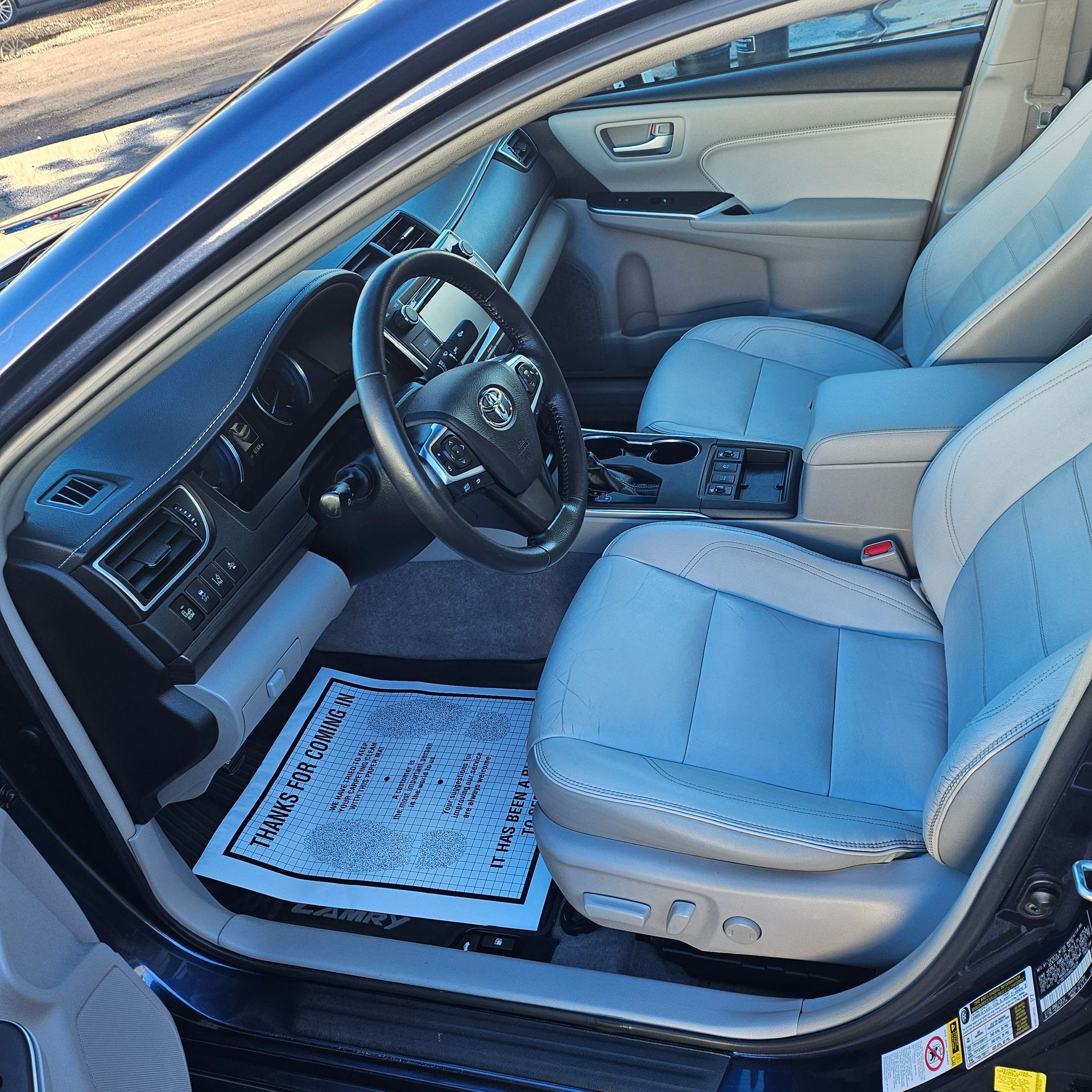 Blue car interior with beige leather front seats, steering wheel, center console, and open driver door