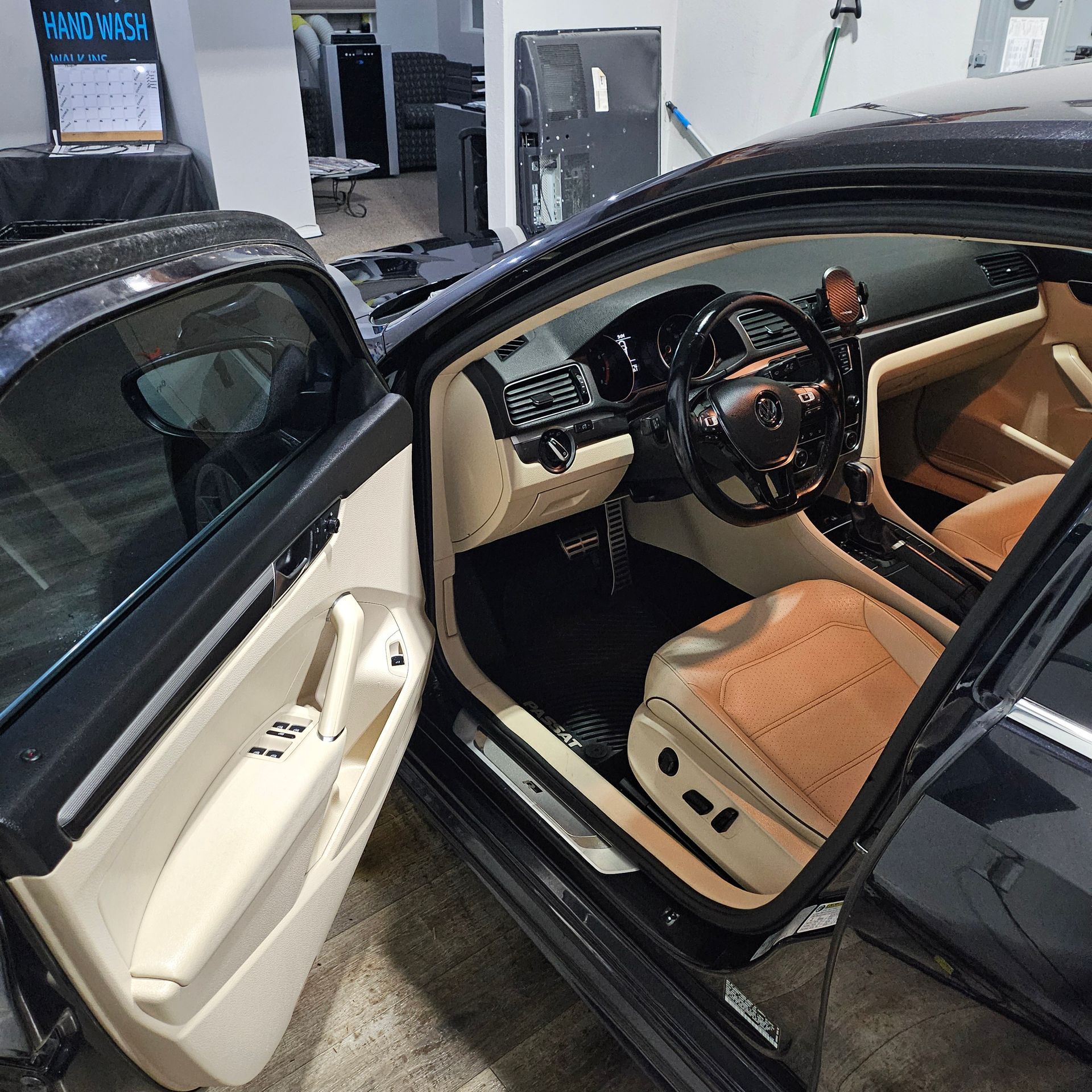 Luxury car interior with tan seats and wood-trim steering wheel, viewed through an open door
