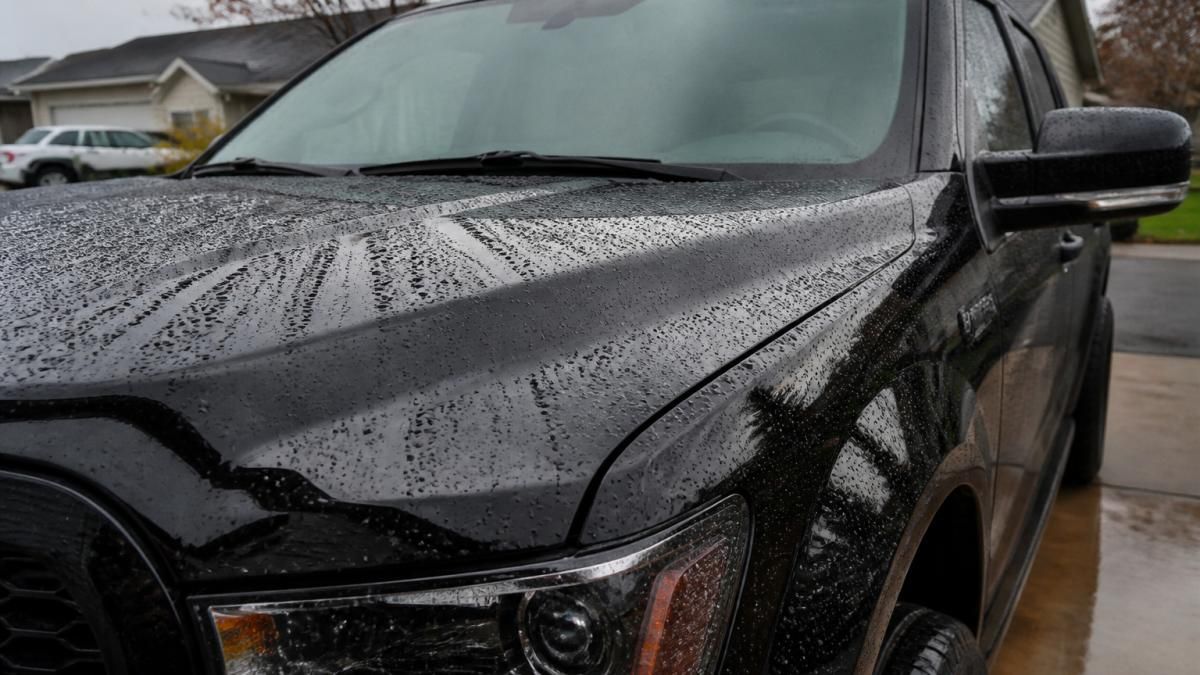 A clean pickup truck parked in a driveway with water beading on the hood after a recent rain, showing the hydrophobic surface