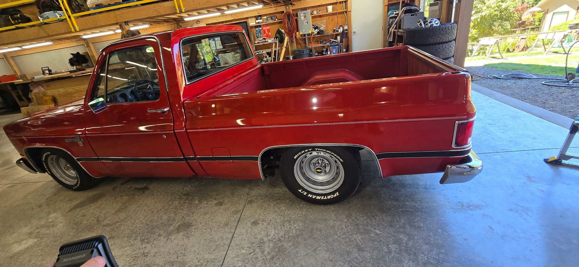 Red classic convertible car in a garage, viewed from the front-left.