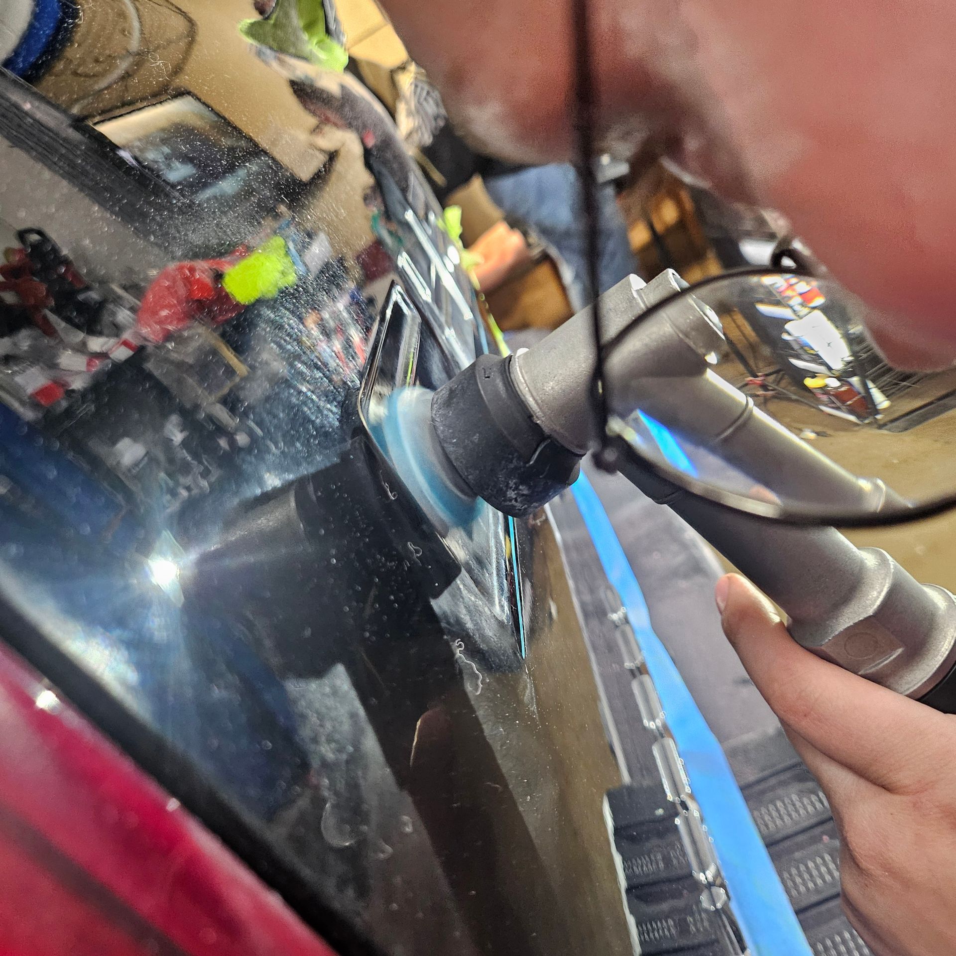 Close-up of a hand using a metal tool on a shiny black car body near a headlight.