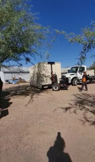 Utility truck and trailer parked in a dusty lot, with a person standing beside them under a blue sky.