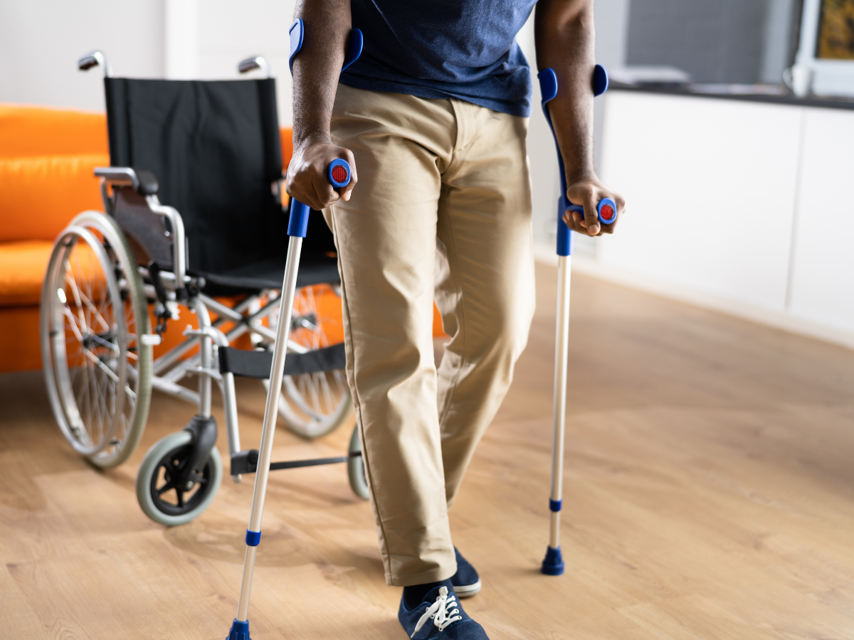 Person using crutches beside a wheelchair in a bright room