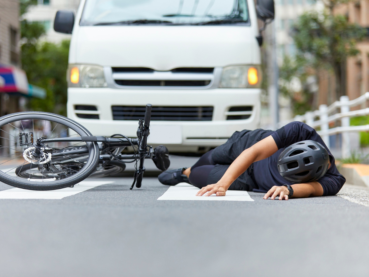 Cyclist lying on road beside a fallen bike as a white van approaches in the background