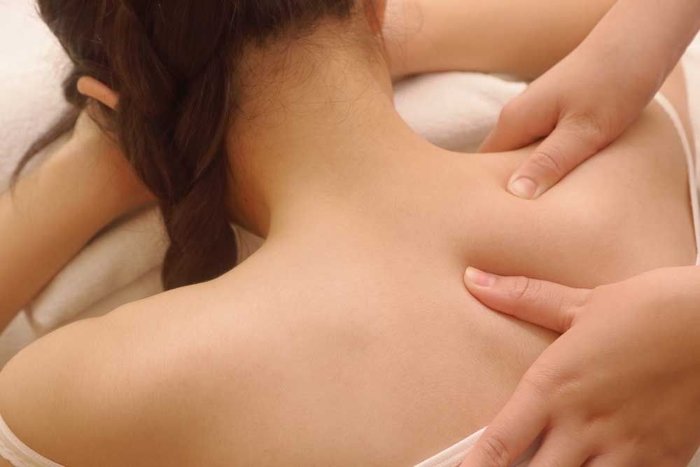 Close-up of a person receiving a back massage on a bed, with hands pressing the shoulders and upper back.