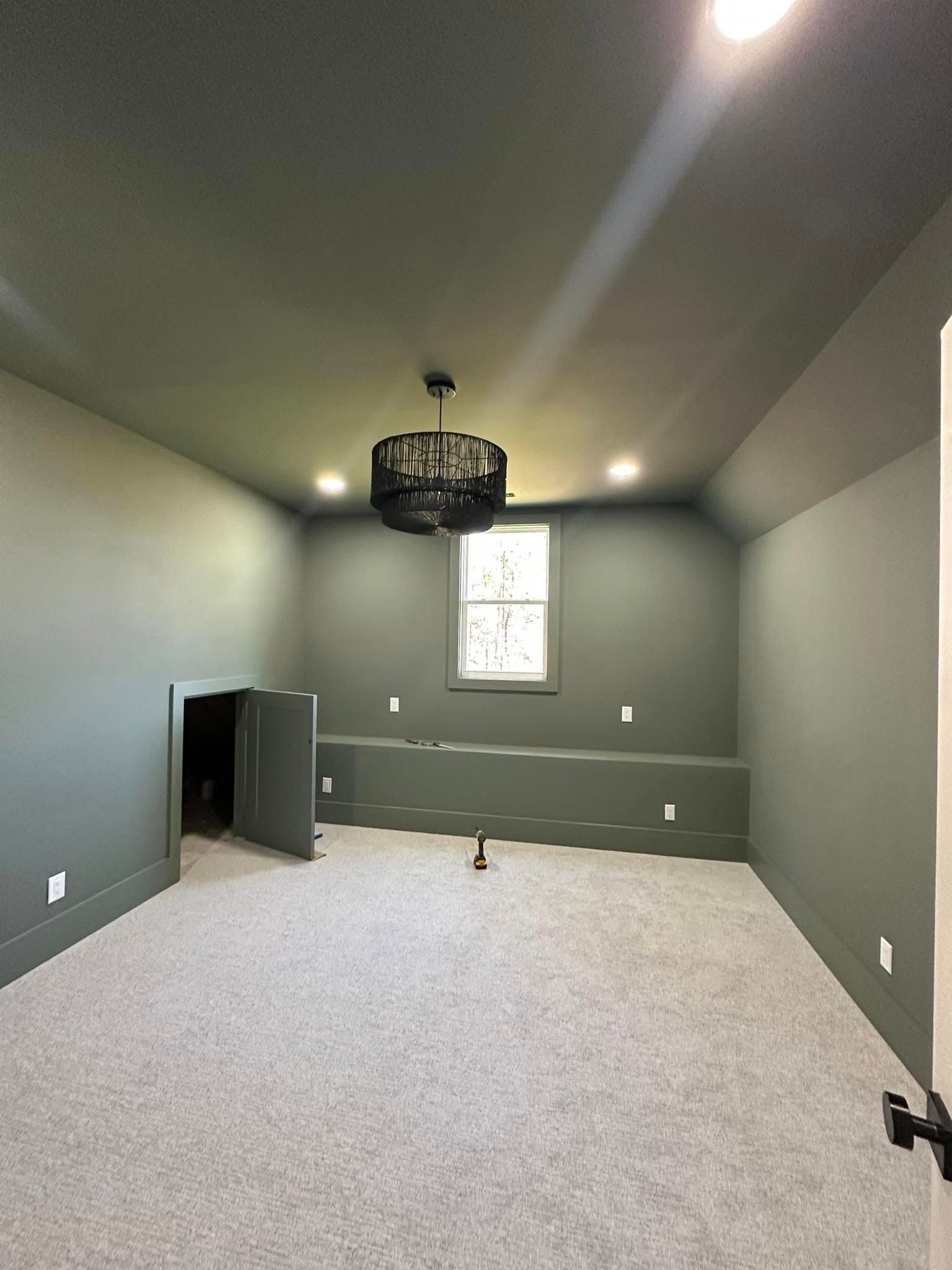 Gray room with a black chandelier, window, and a small doorway.
