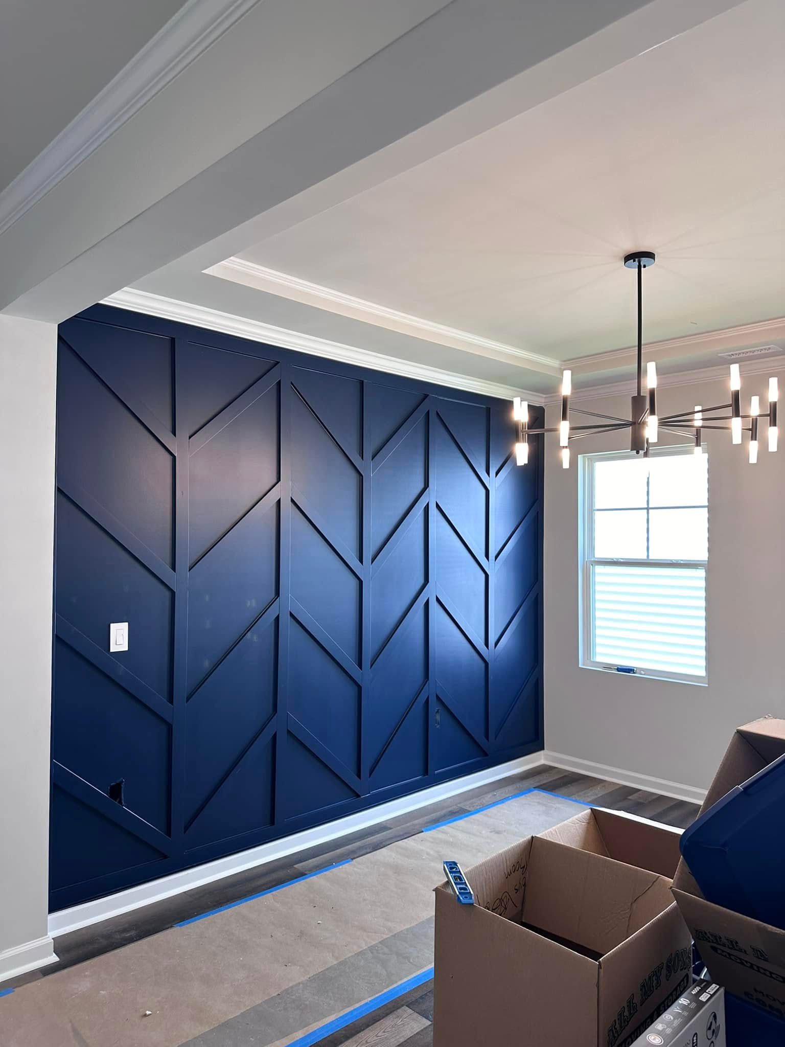 Dark blue geometric accent wall in a room with a chandelier and window.