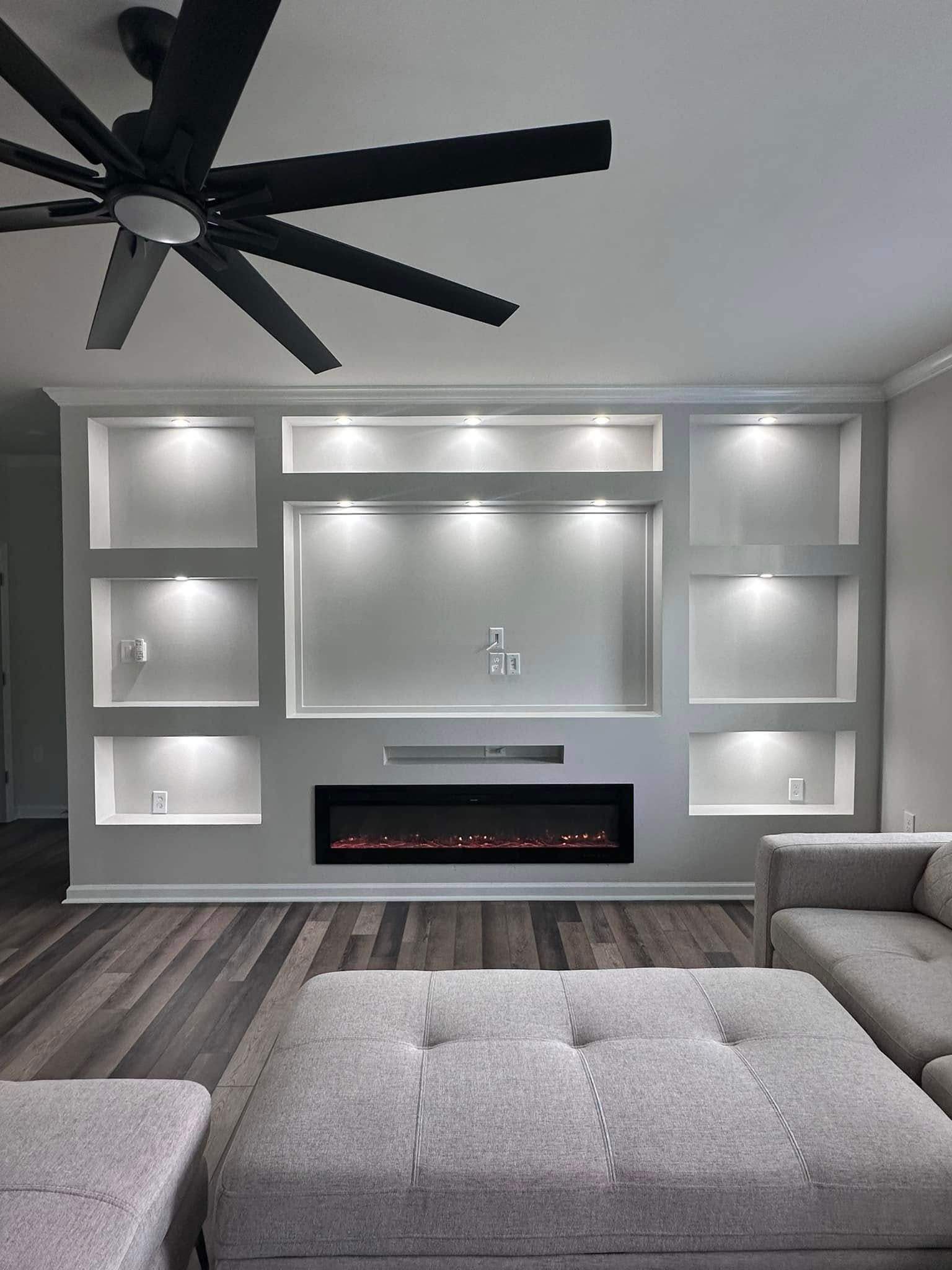 Built-in white media center with fireplace, shelves, and recessed lighting. A gray sectional sofa sits in front.