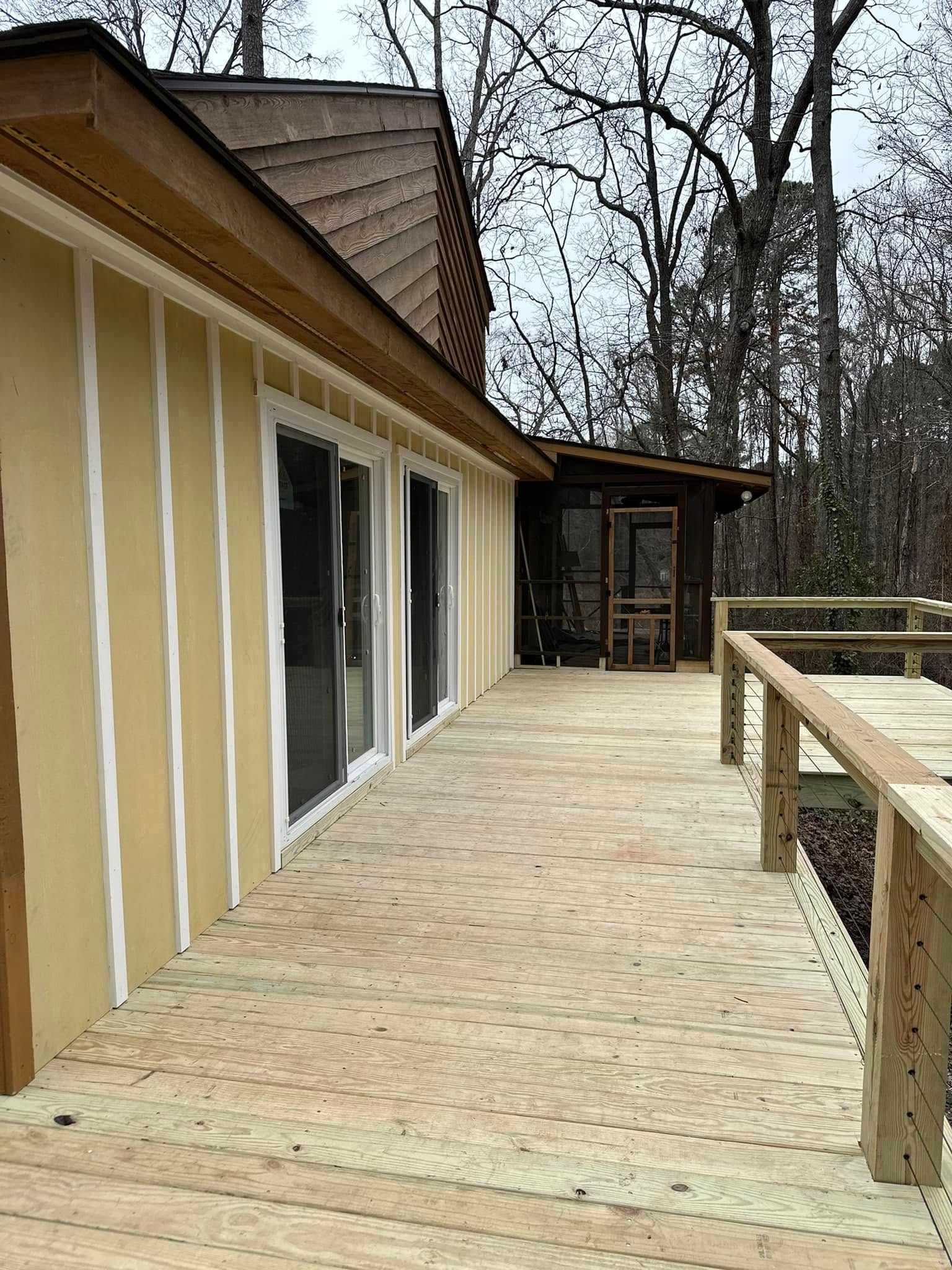 Deck leads to a home with yellow siding, sliding glass doors, and a screened porch.