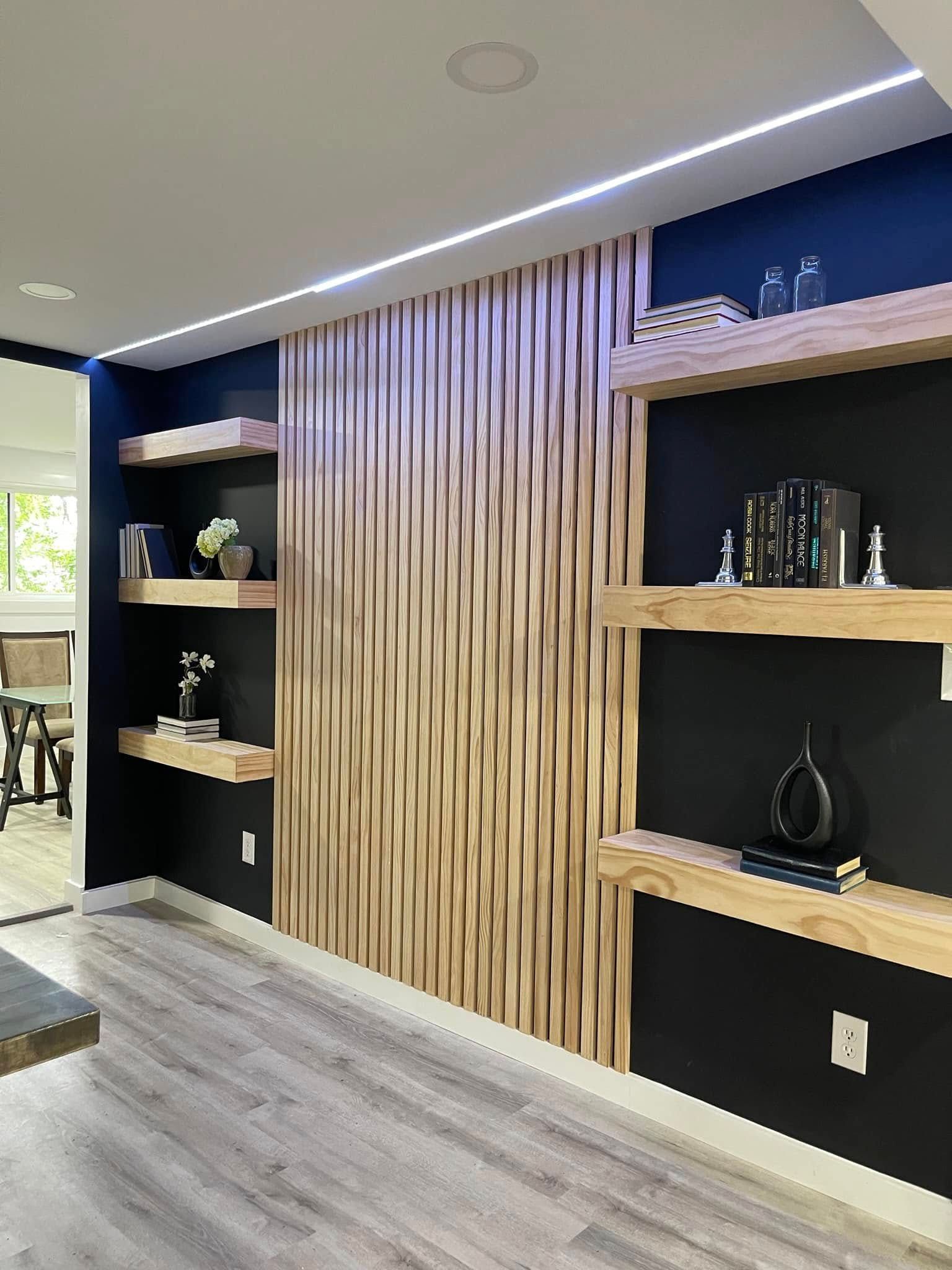 Wooden slatted wall with floating shelves against dark blue walls. Books and decor displayed.