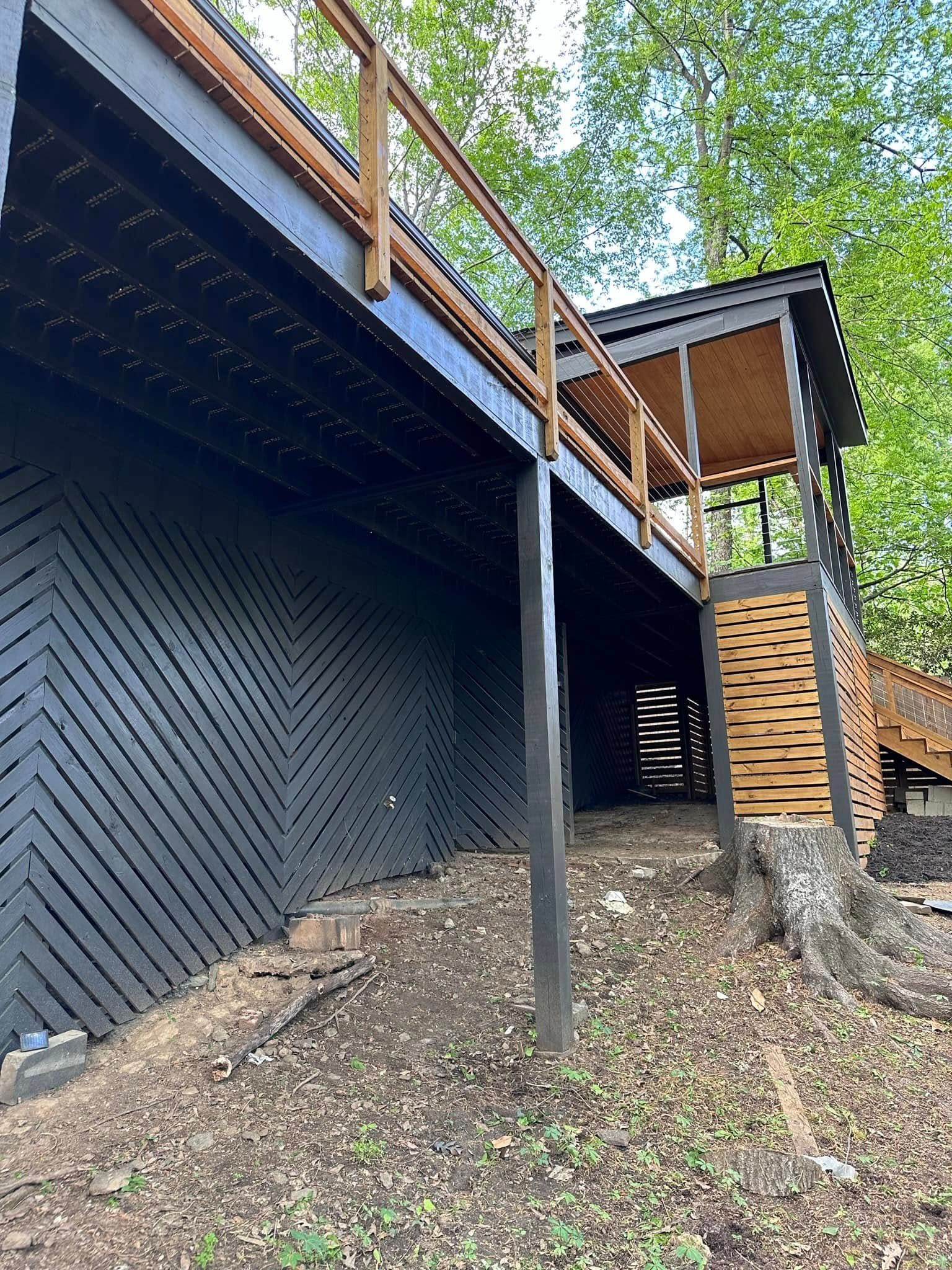Black-painted wooden deck with zigzag design on the side, wooden railings, and trees in the background.