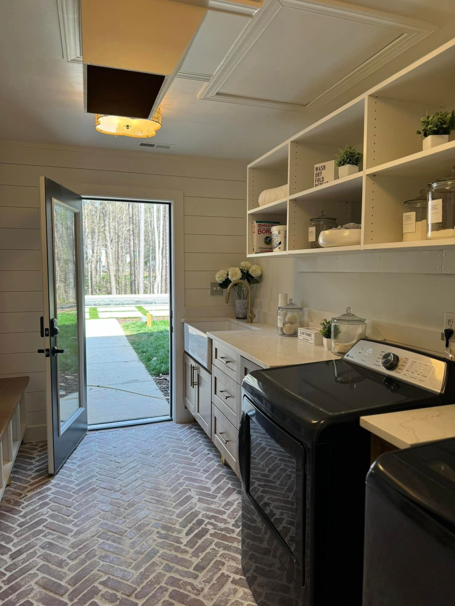 Laundry room with black appliances, white cabinets, open door to outdoors, and patterned rug.