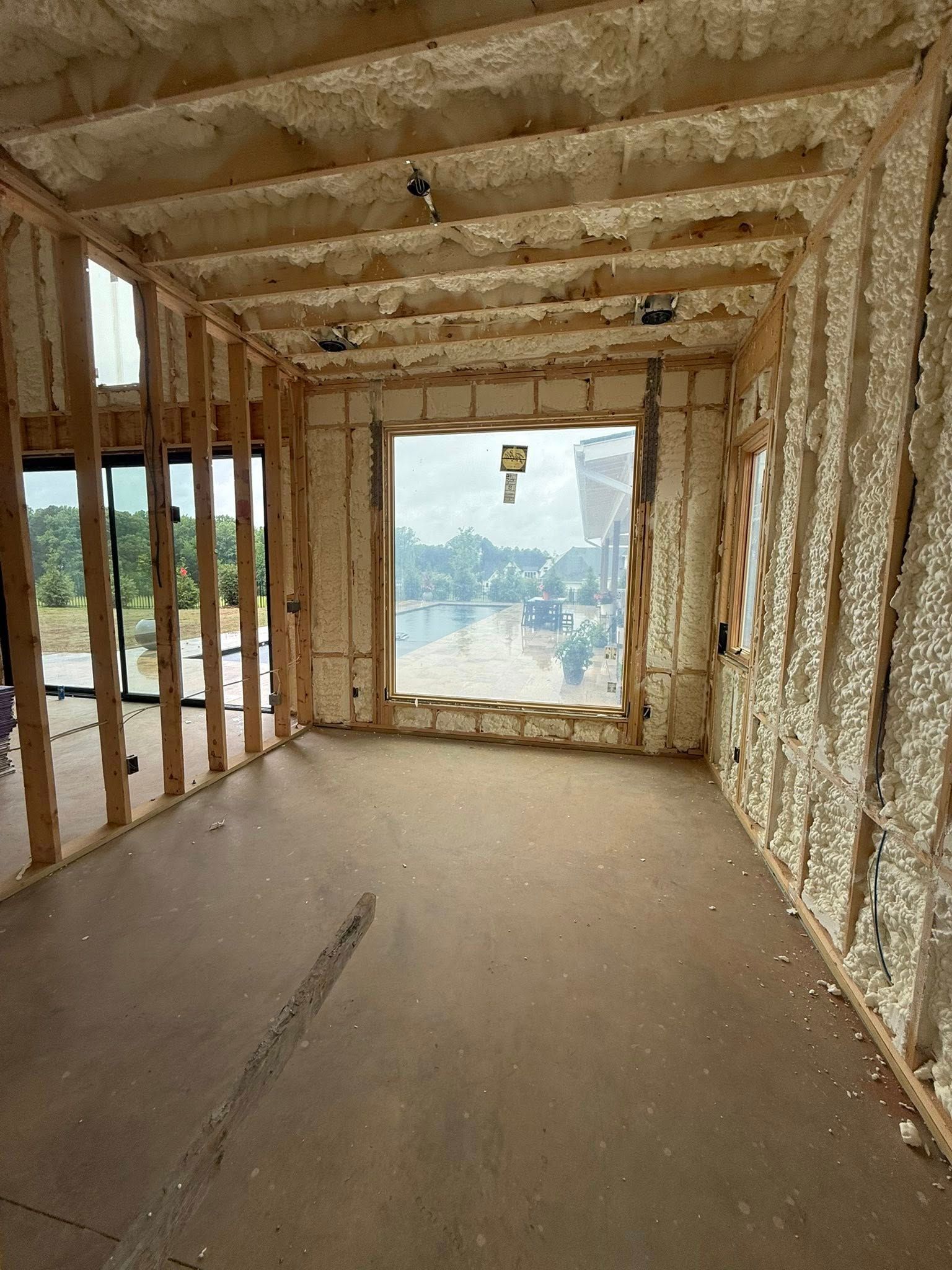 Interior view of a room under construction, with exposed wooden frame and spray foam insulation. Window overlooks a view.