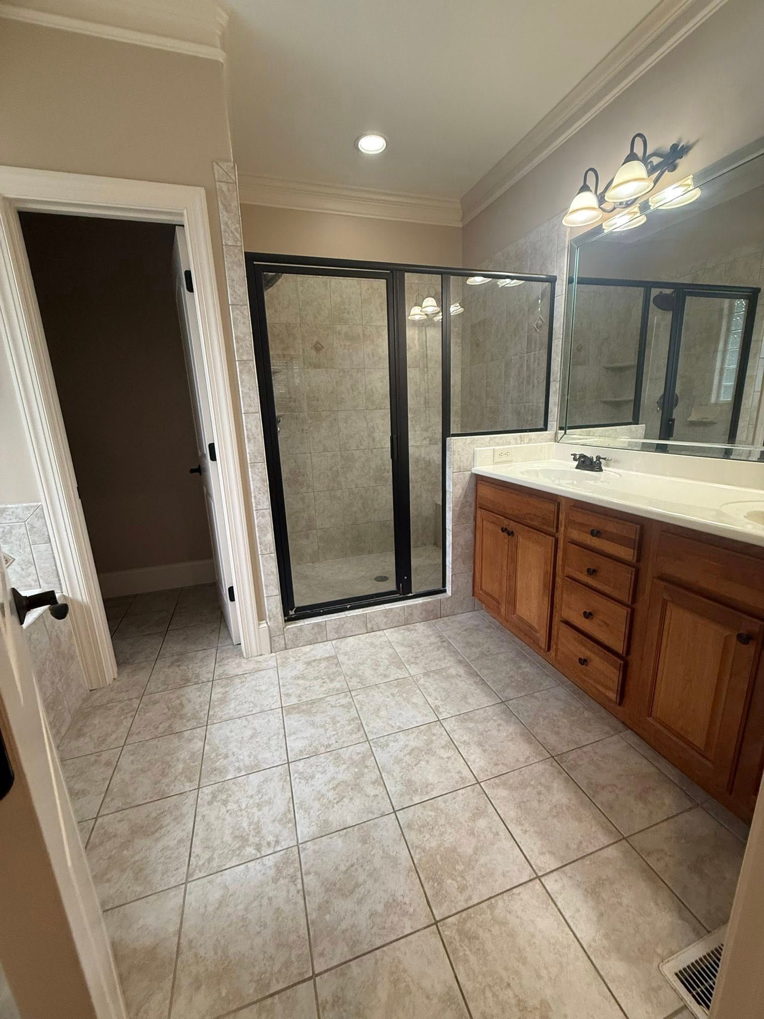 Bathroom with a black-framed shower, wooden vanity, and tiled floor.