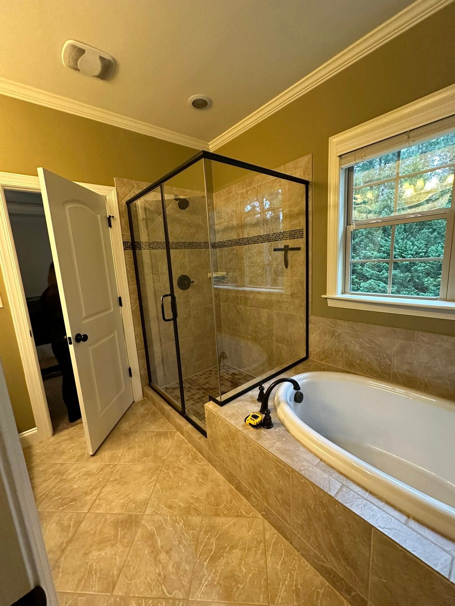 Bathroom with glass shower, bathtub, and door. Beige tile floor and light green walls.