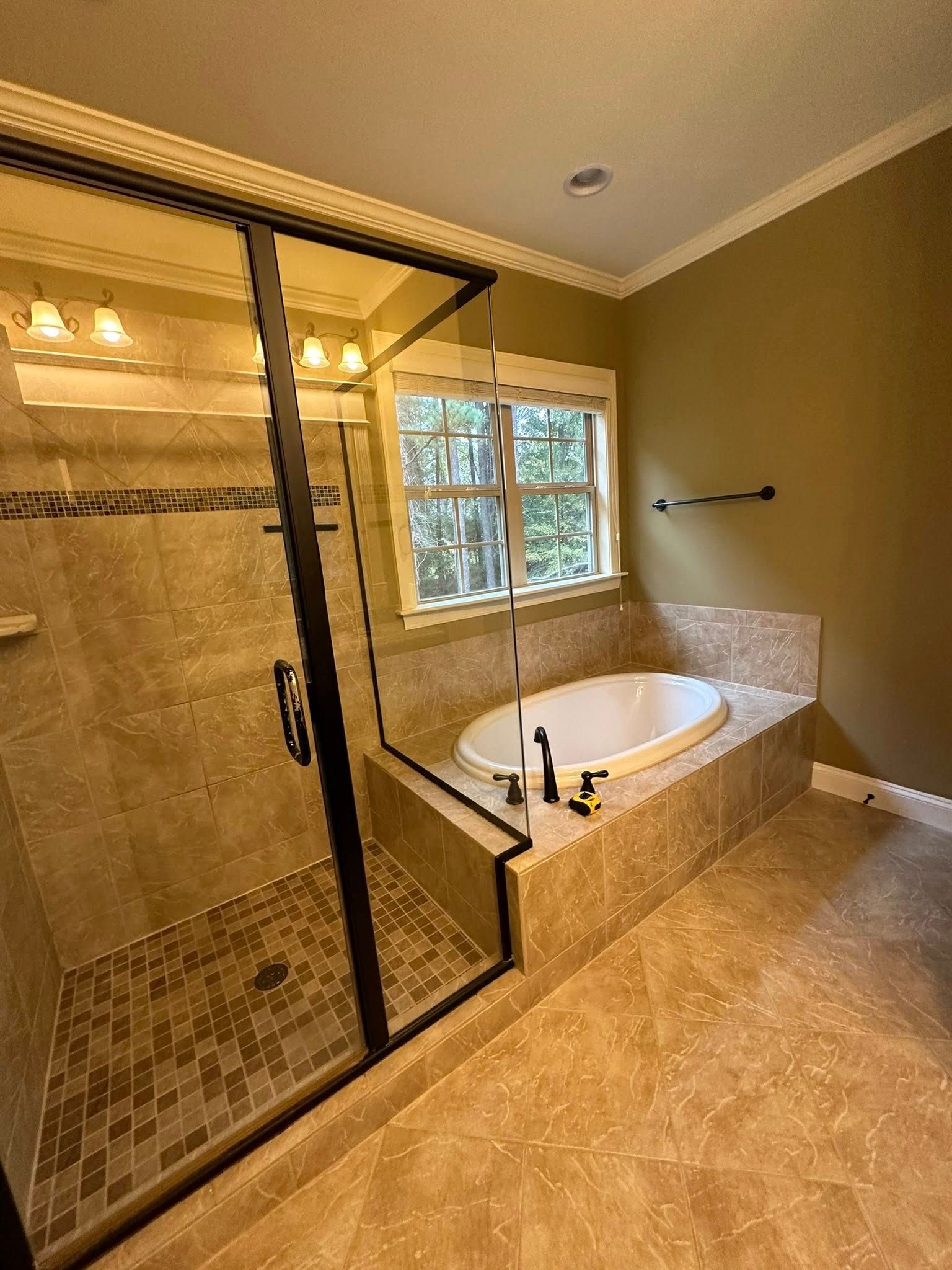 Bathroom with a walk-in shower and built-in bathtub. Beige tile and trim. Black shower door frame. Window.