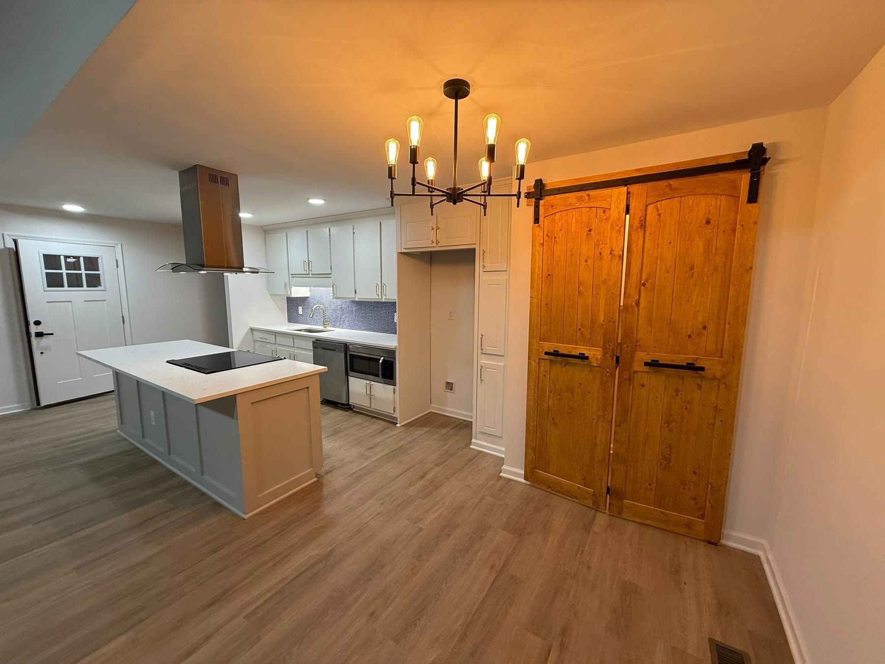 Modern kitchen with island, stainless steel appliances, light wood floors, and barn doors.