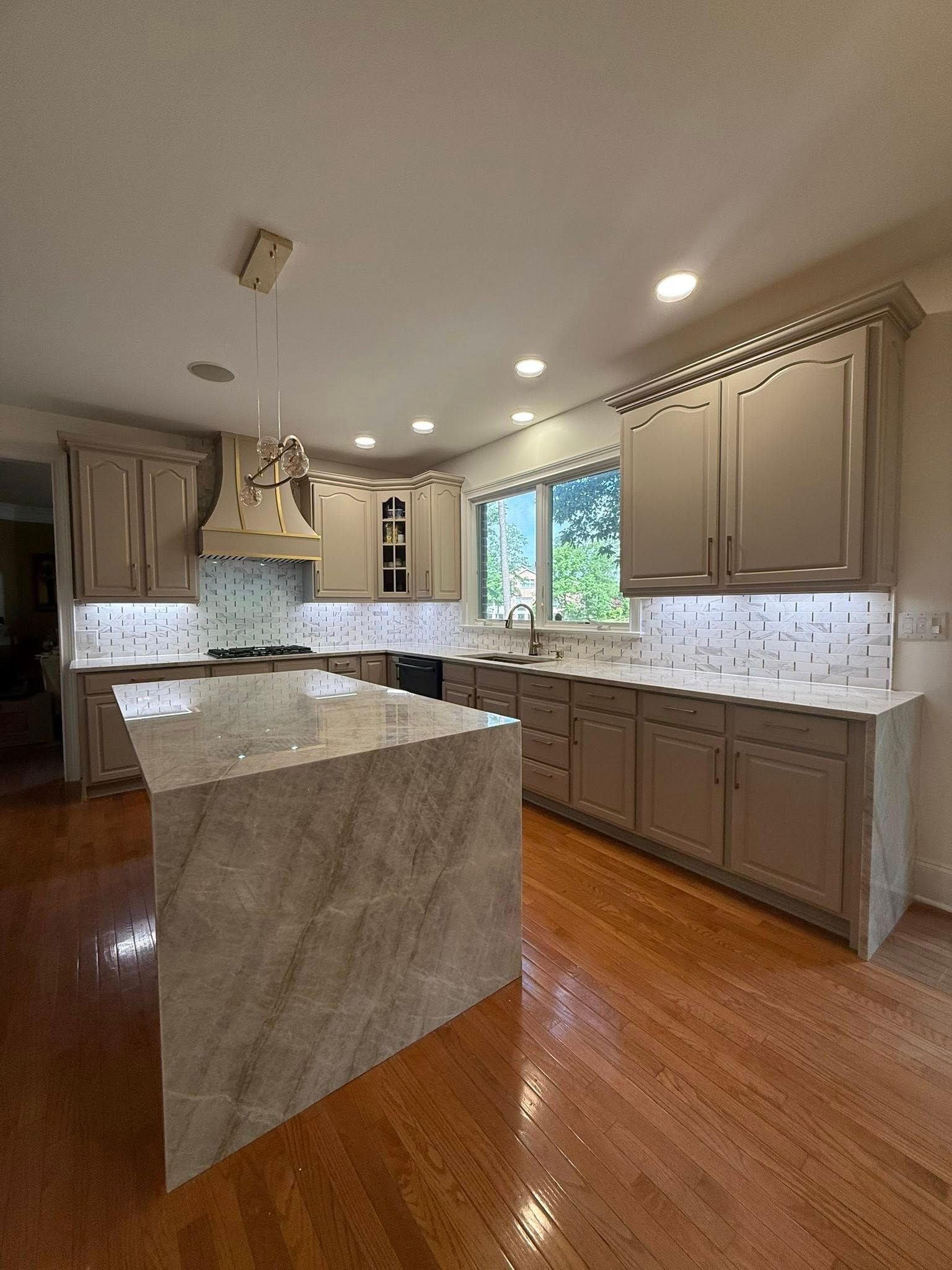 Kitchen with gray cabinets, marble countertops, island, and wooden floor.