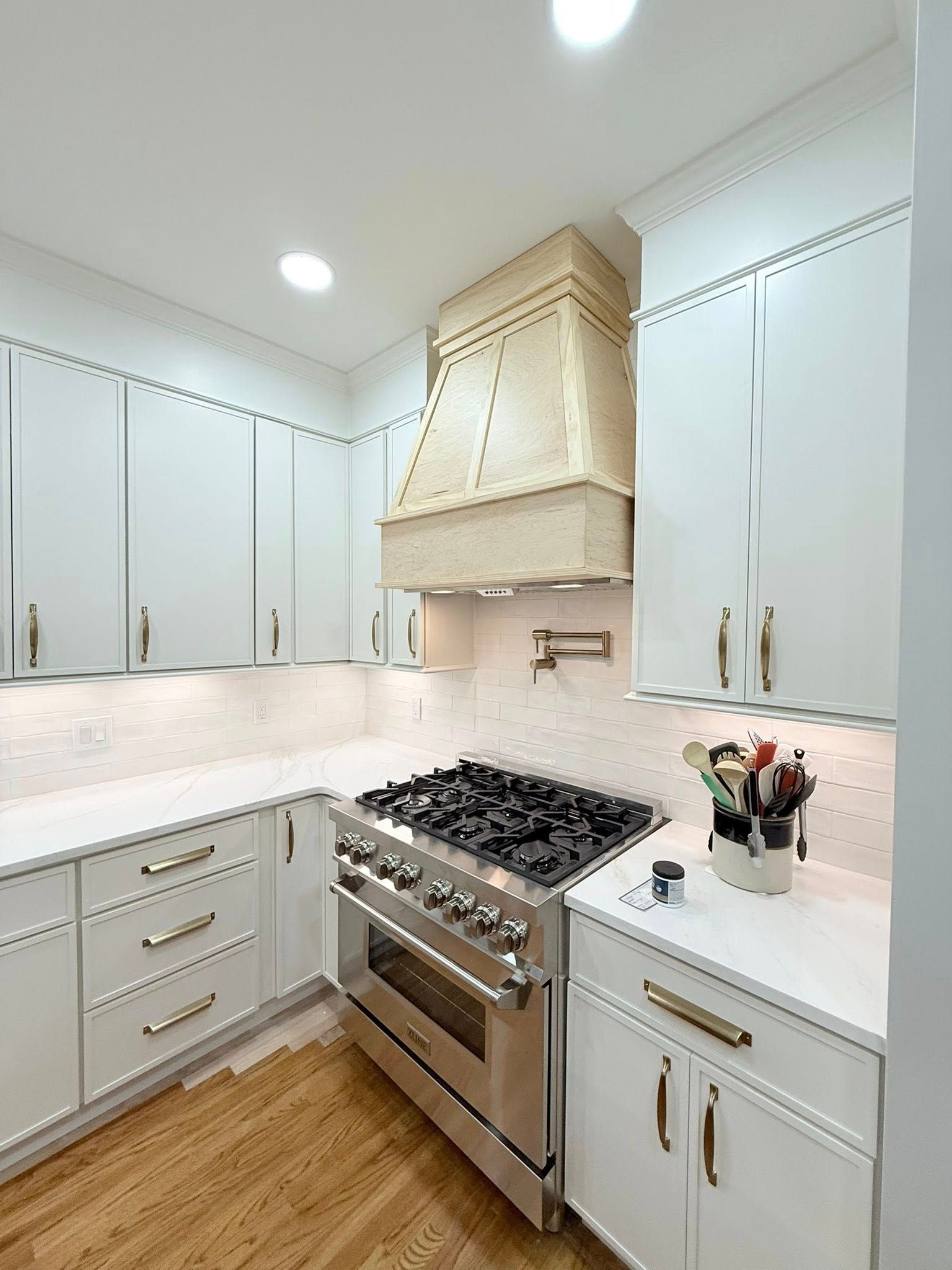 White kitchen with stainless steel stove, cabinets, and light wood flooring.