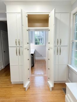 White kitchen cabinets with open doors leading to a doorway and window.